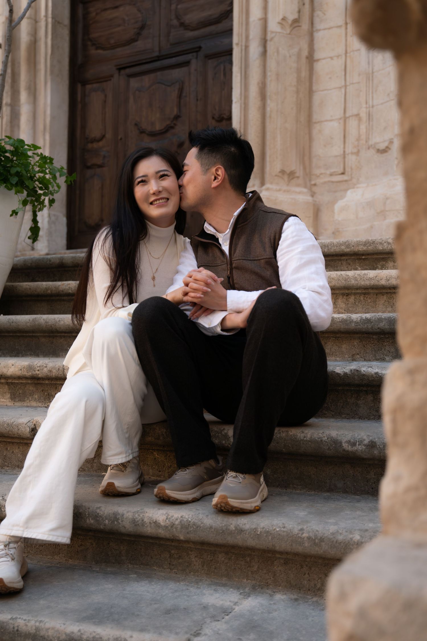 A couple sits intimately on stone steps of a historic building.