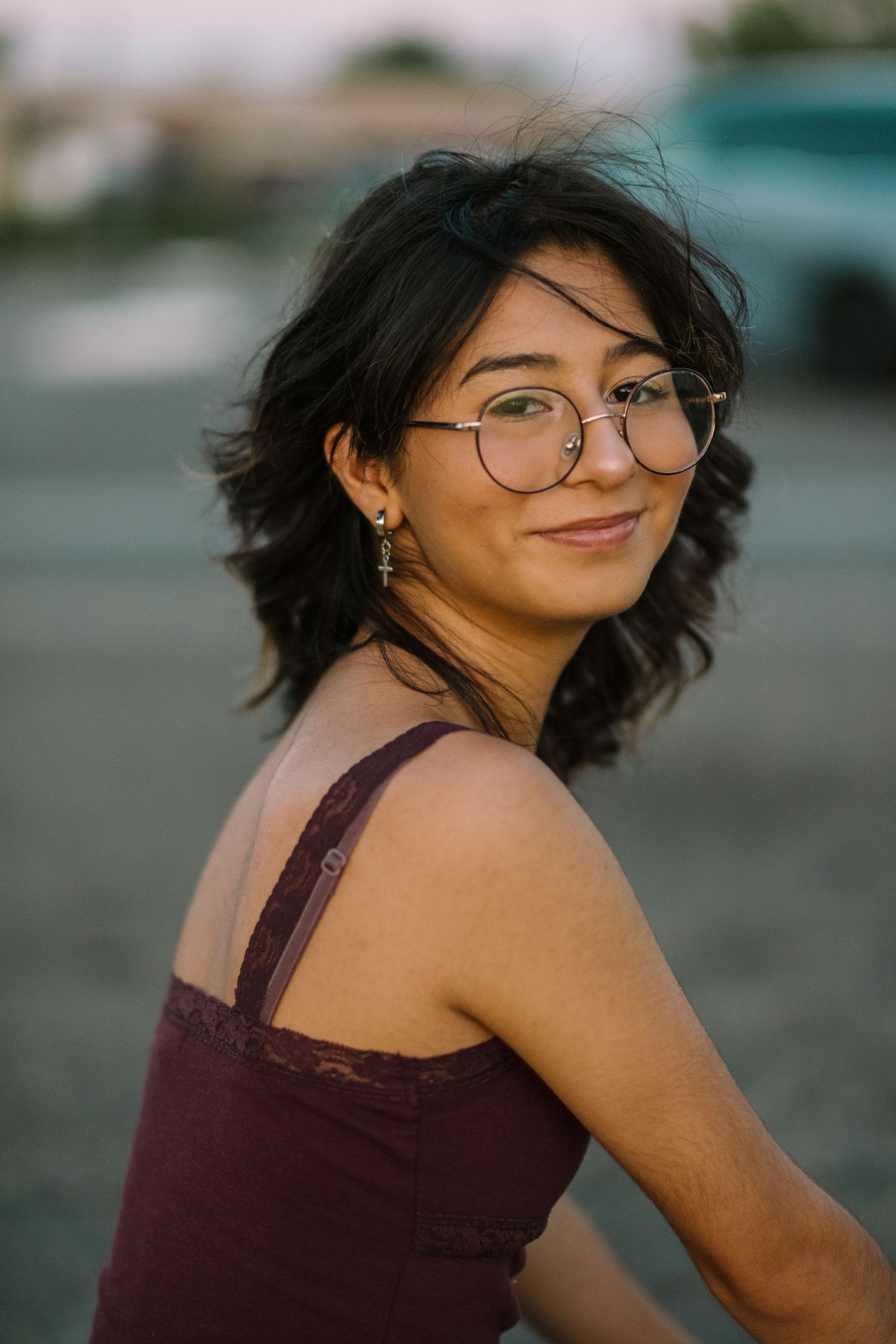 A person in a maroon top poses with windswept hair during an outdoor photoshoot.