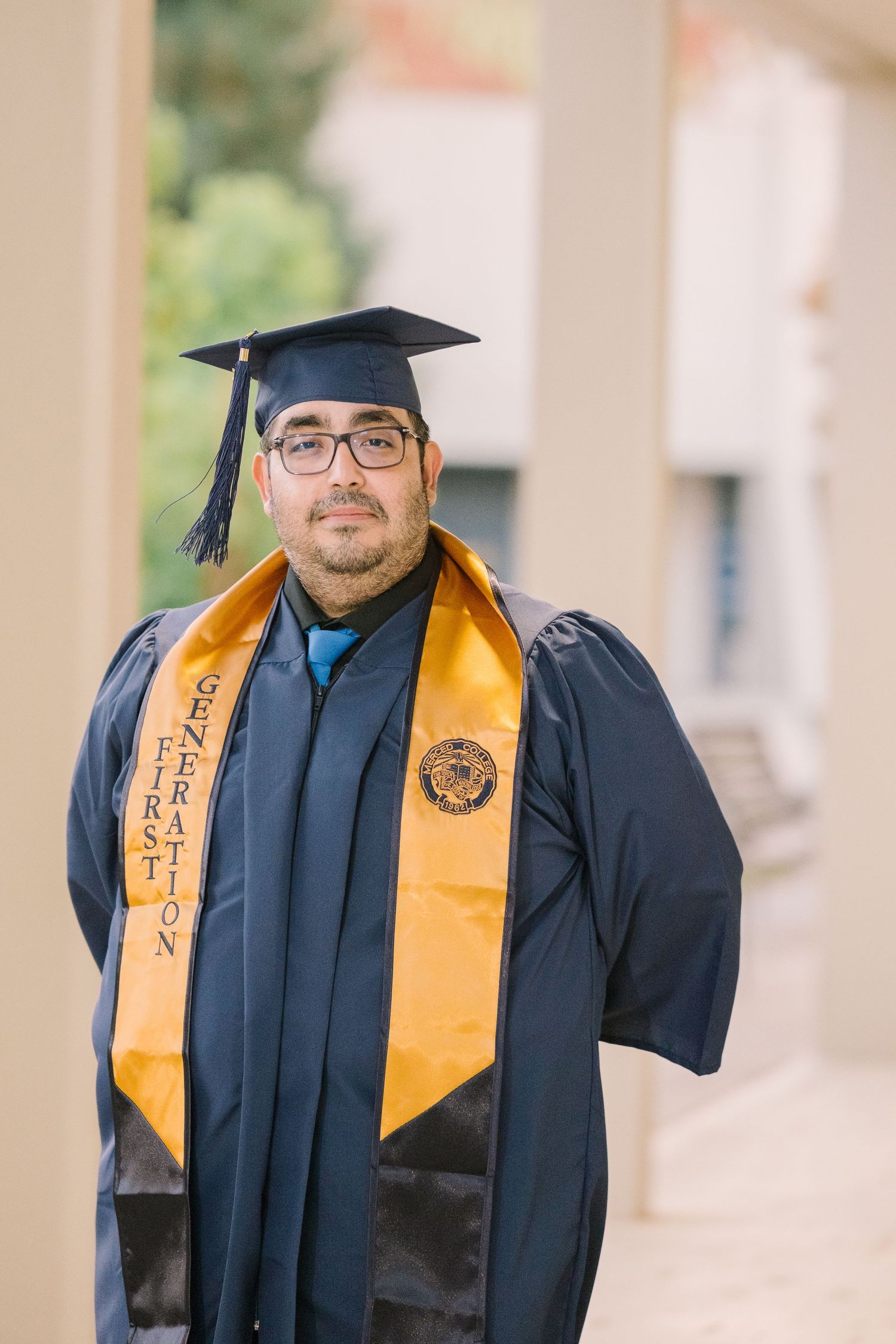 A graduate in blue cap and gown with gold honors stole poses for graduation photos.