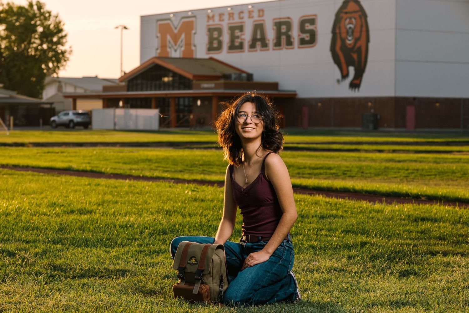 Person sitting in golden hour sunlight on grassy field wearing teal pants and black top.
