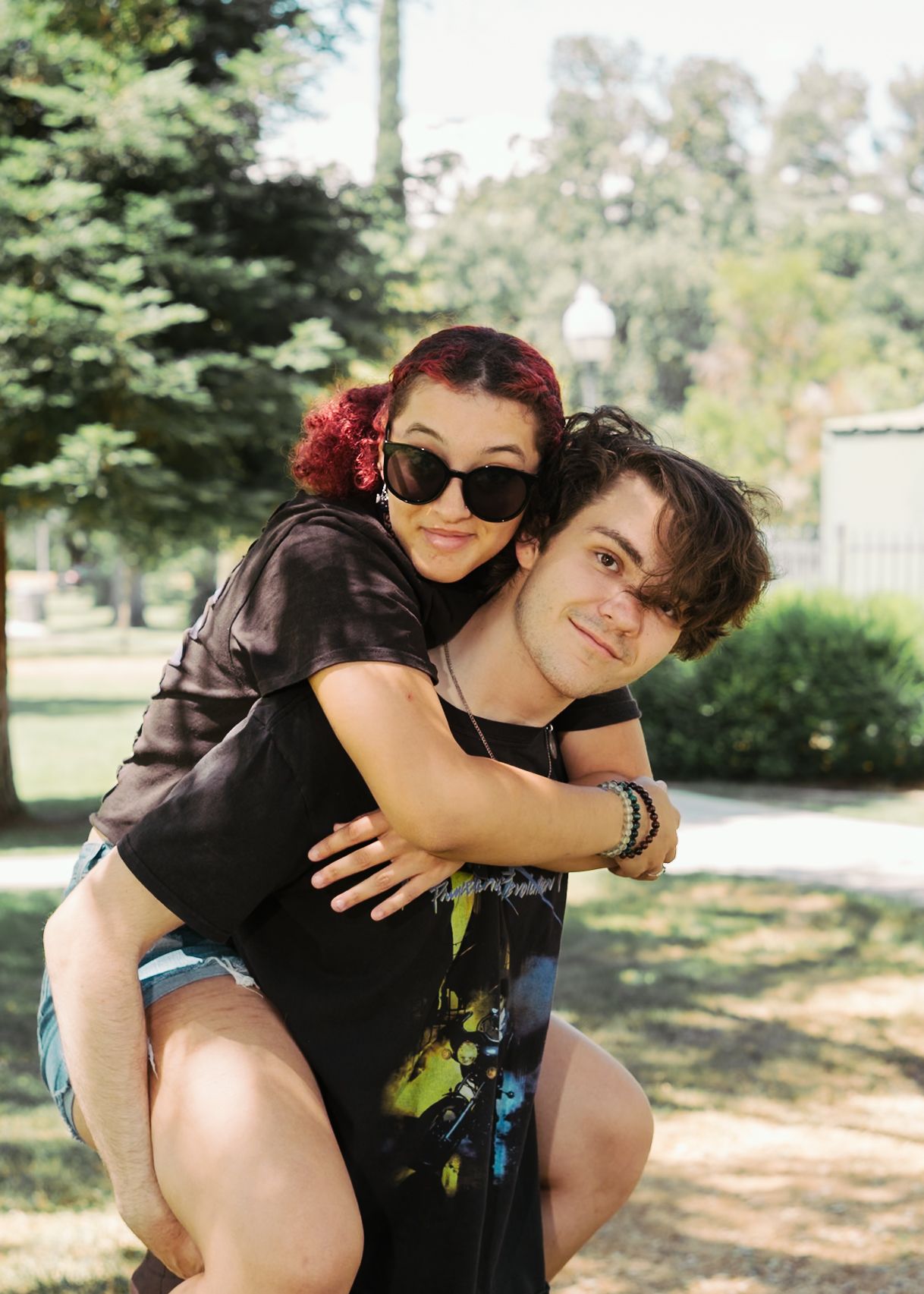 Playful outdoor photoshoot with couple enjoying piggyback ride in park setting.