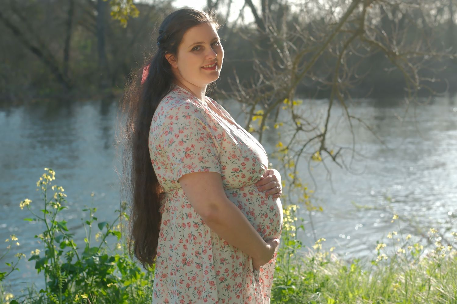 Maternity photoshoot by riverside with floral dress and natural lighting.