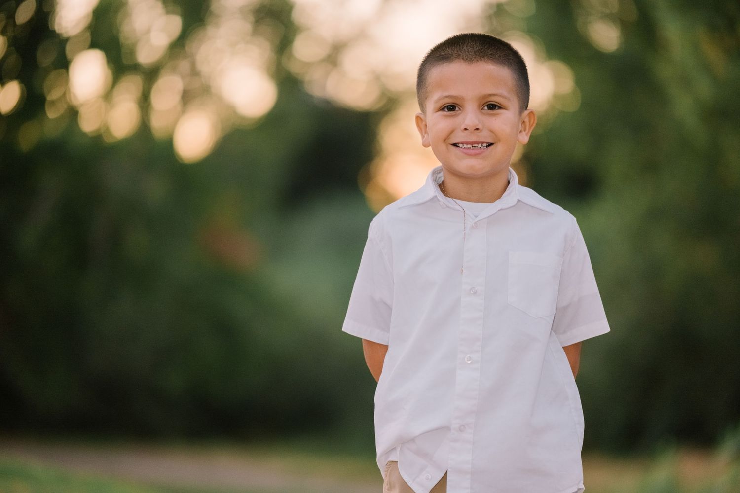 A boy in a white polo shirt smiles warmly during an outdoor portrait session.
