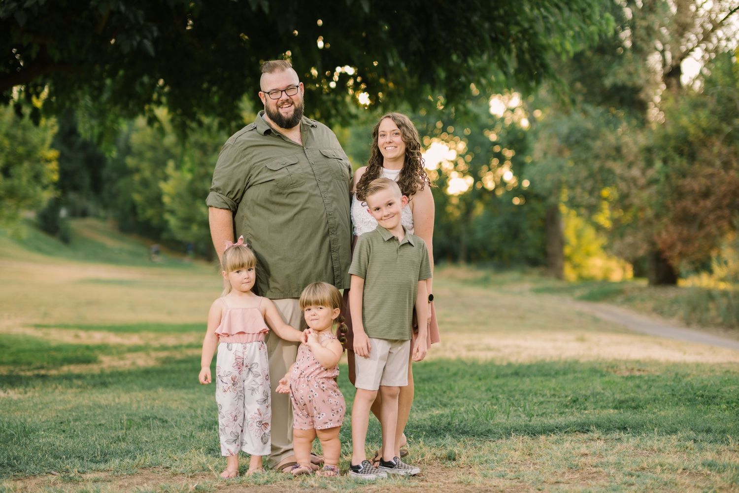 A group poses together on grass at sunset with trees in the background.