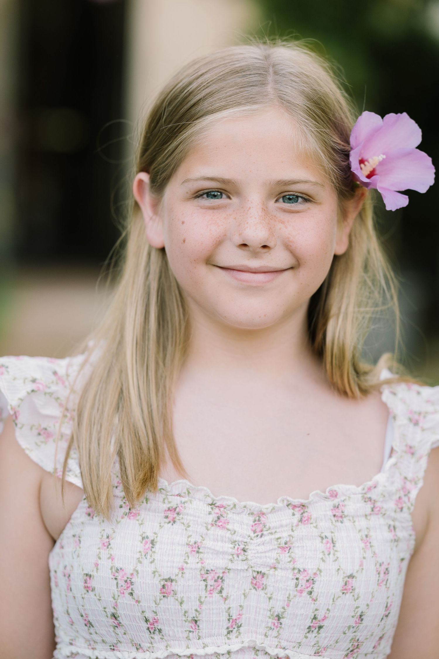 Young girl in floral dress with pink flower hair accessory poses for spring portraits.