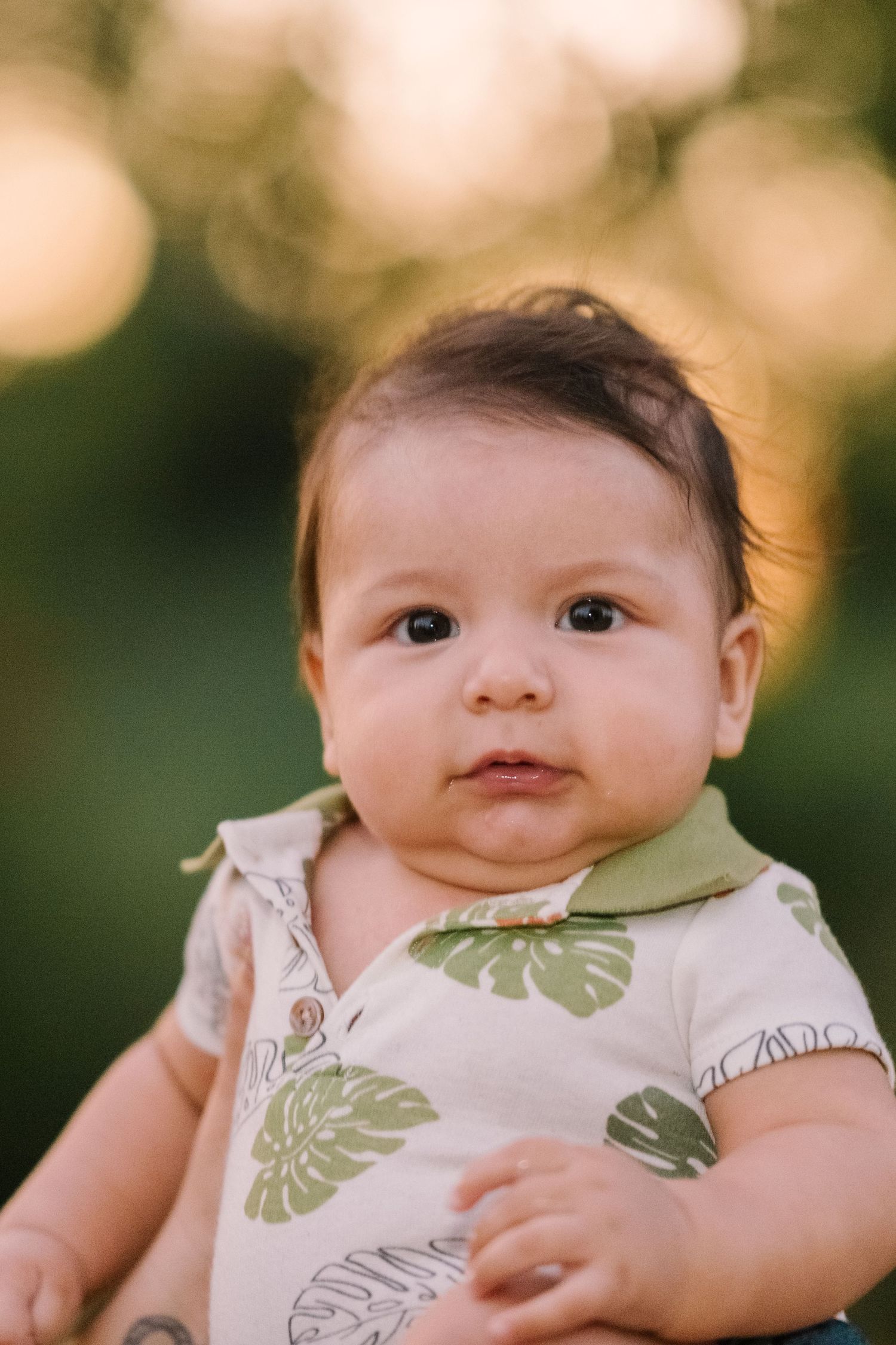 Baby wearing tropical print outfit smiles sweetly during outdoor photo session.