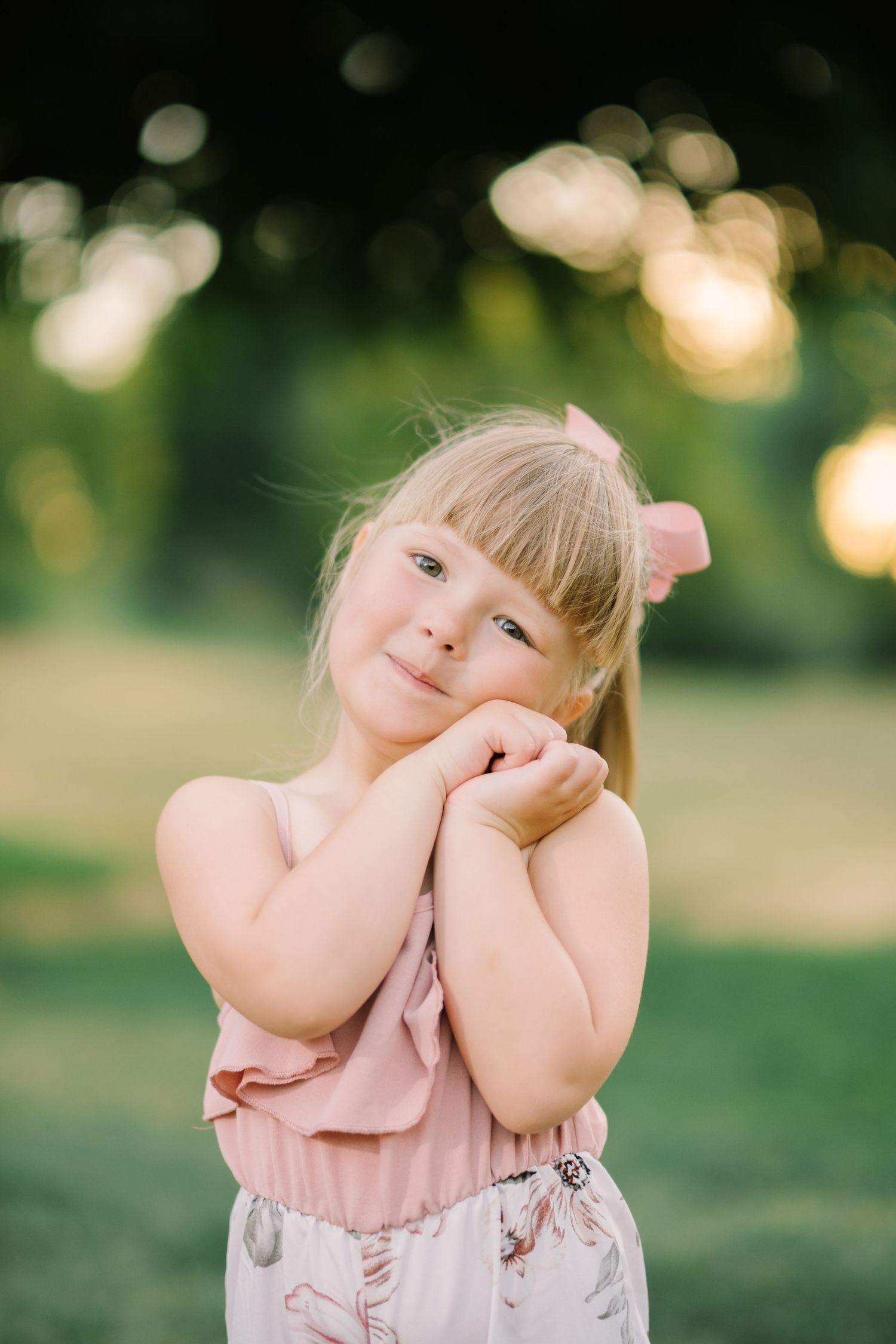 Little girl in pink dress makes playful expressions during outdoor photo session.