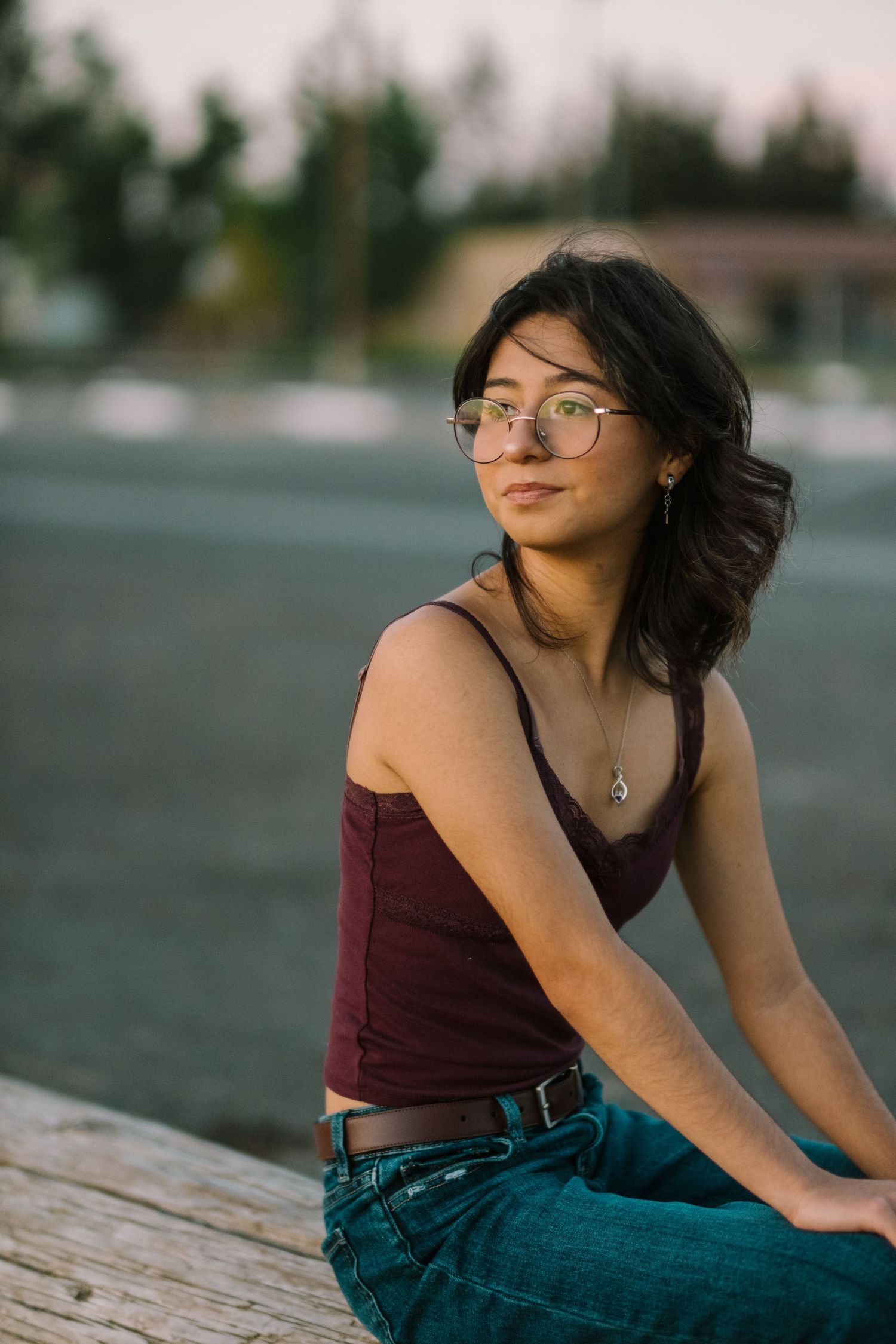 A person in a maroon tank top and jeans poses casually during a sunset photo session.