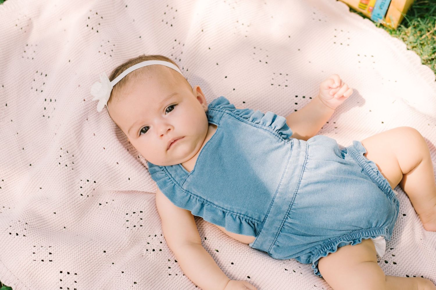 Baby lying on pink floral blanket during outdoor photography session.