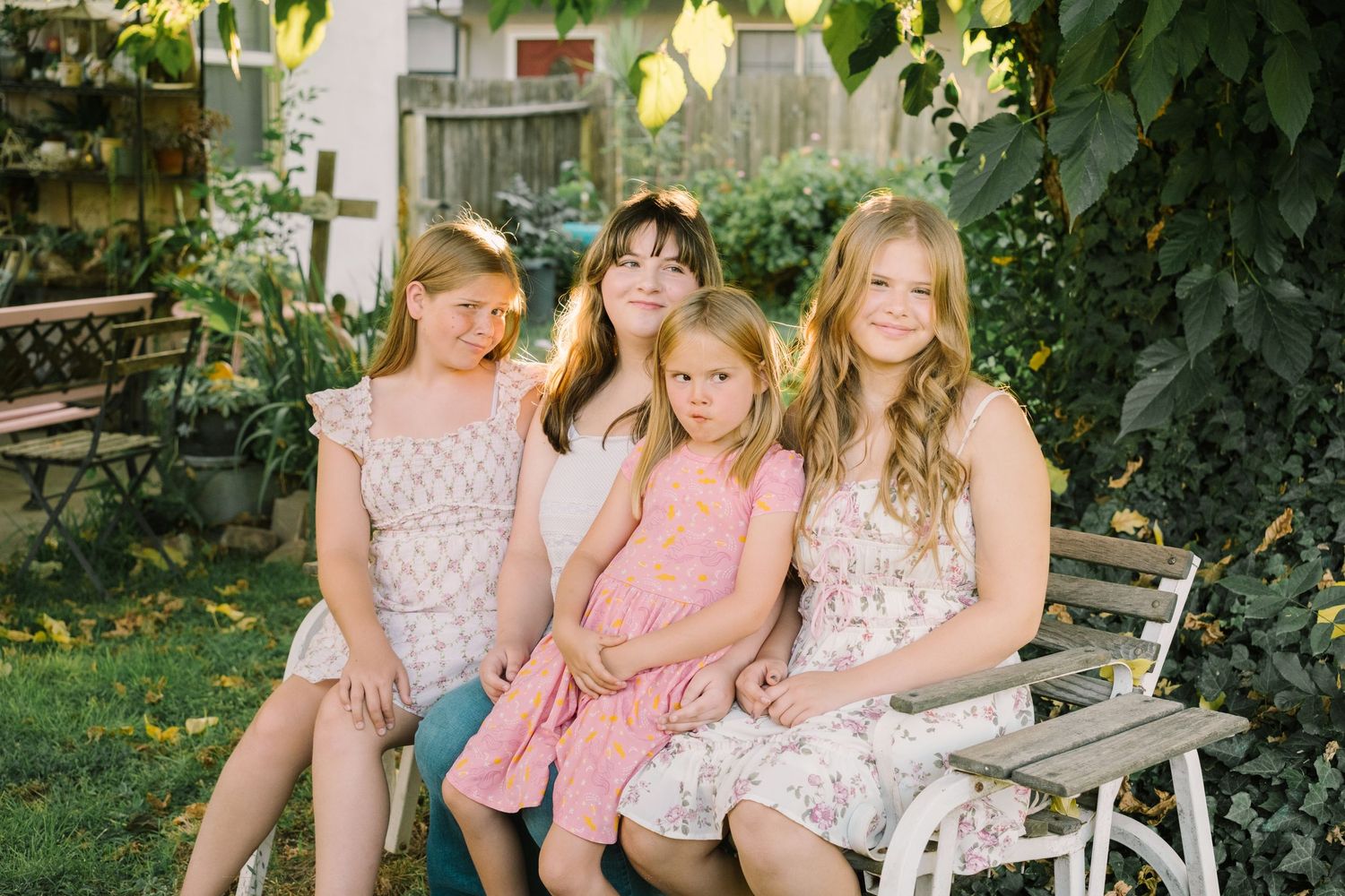 Three friends pose together in front of green foliage on a white bench in a garden setting.