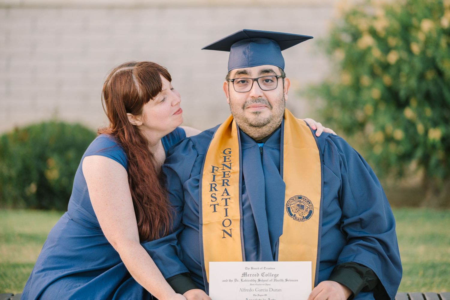 A graduate in blue cap and gown poses with loved ones during commencement celebrations.