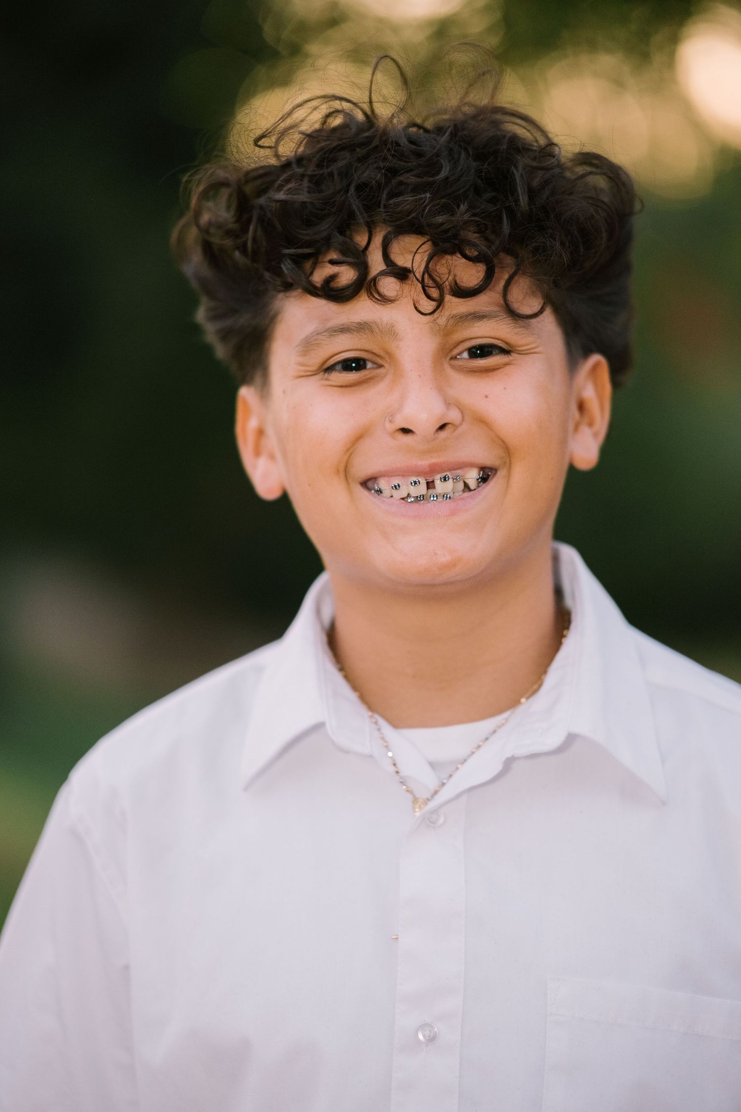 A child in a white shirt smiles brightly showing braces during an outdoor photo session.
