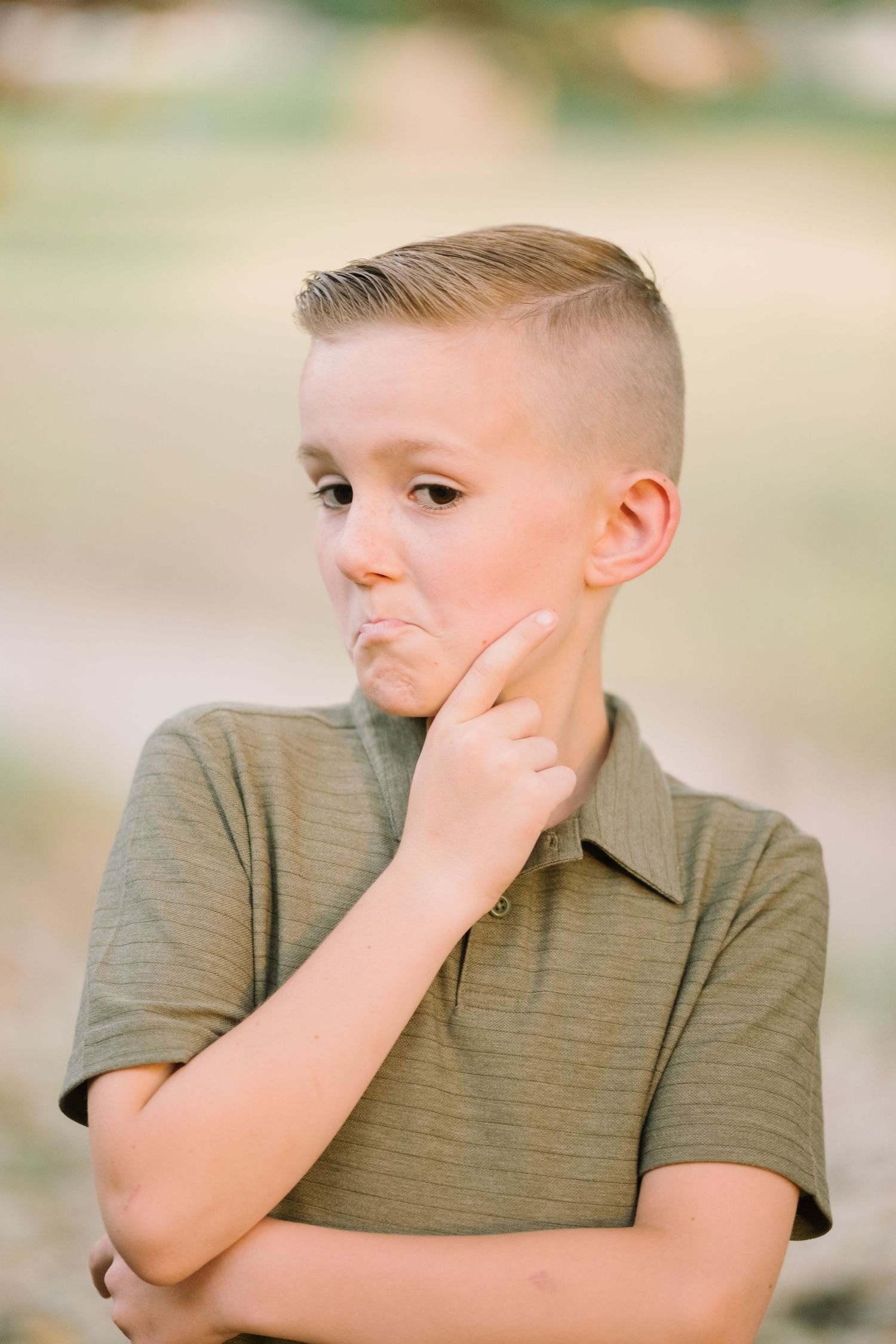 Young boy in olive polo shirt posing thoughtfully for outdoor portraits.