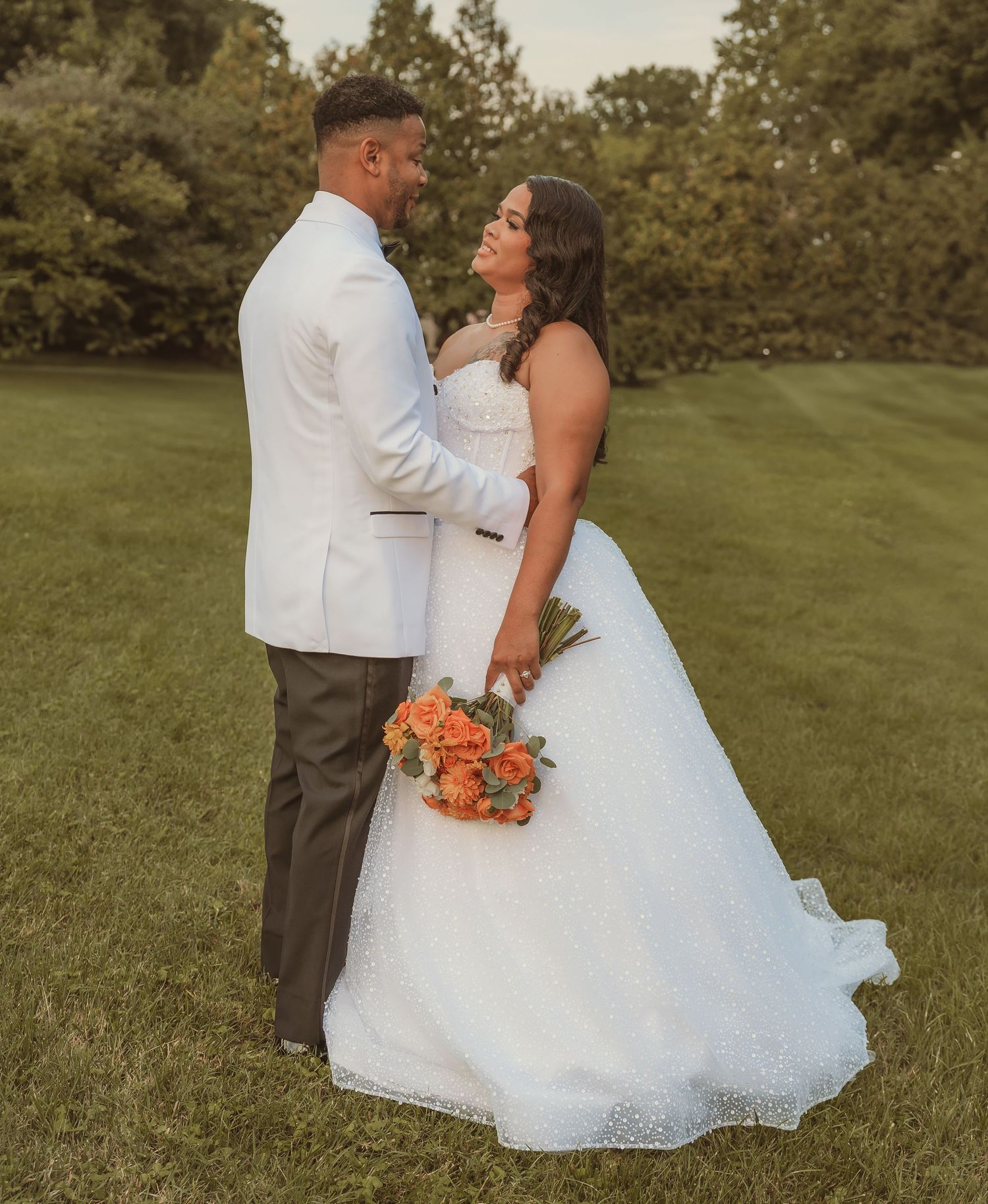 Wedding couple poses for romantic portraits on a green lawn at sunset.