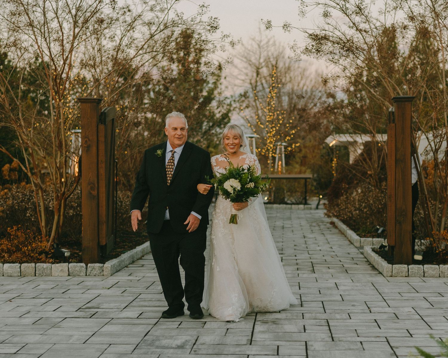 A couple walks together on a stone patio during an outdoor winter wedding ceremony.