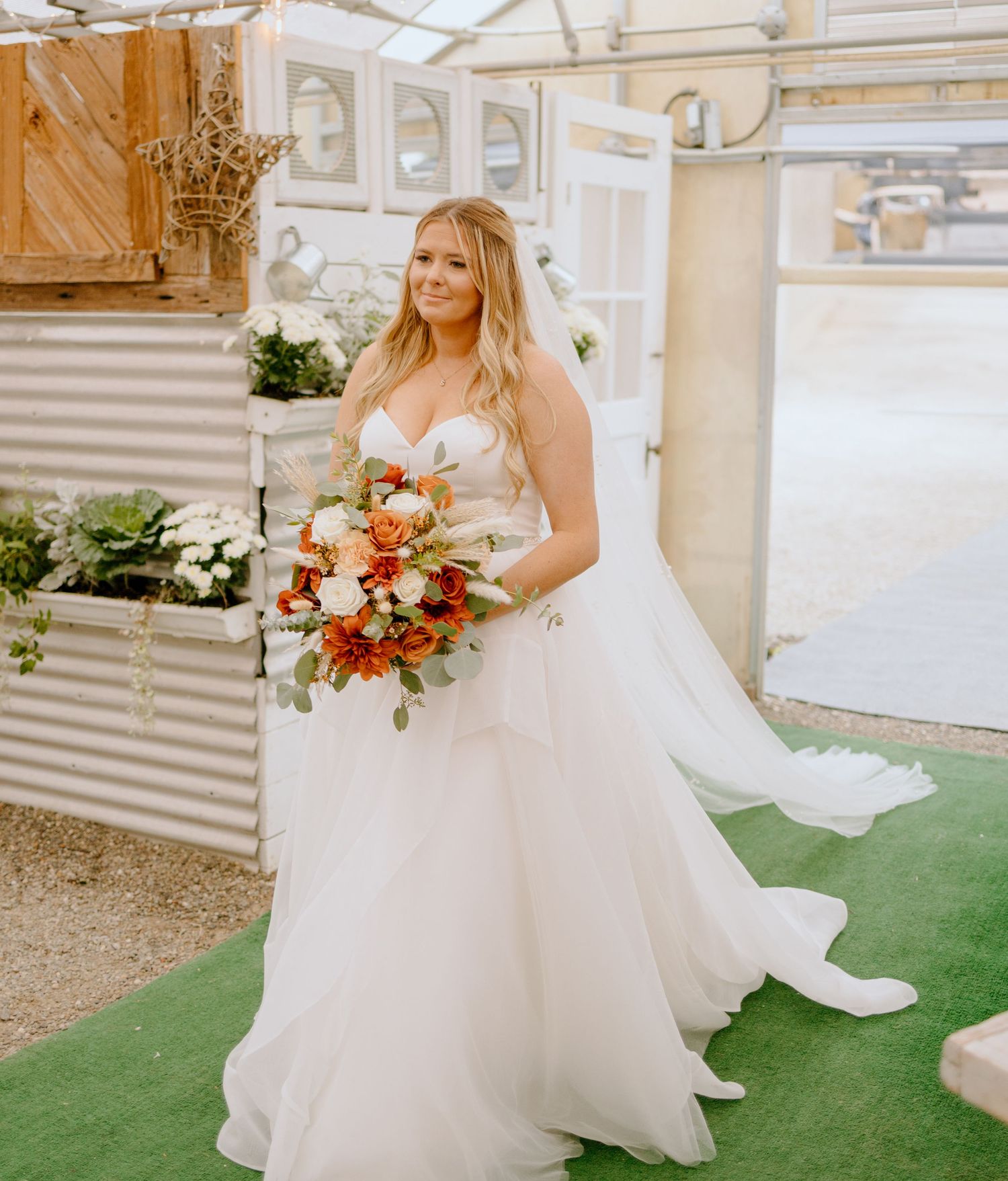 A bride in a flowing white ballgown wedding dress walks gracefully on grass while holding a colorful floral bouquet.
