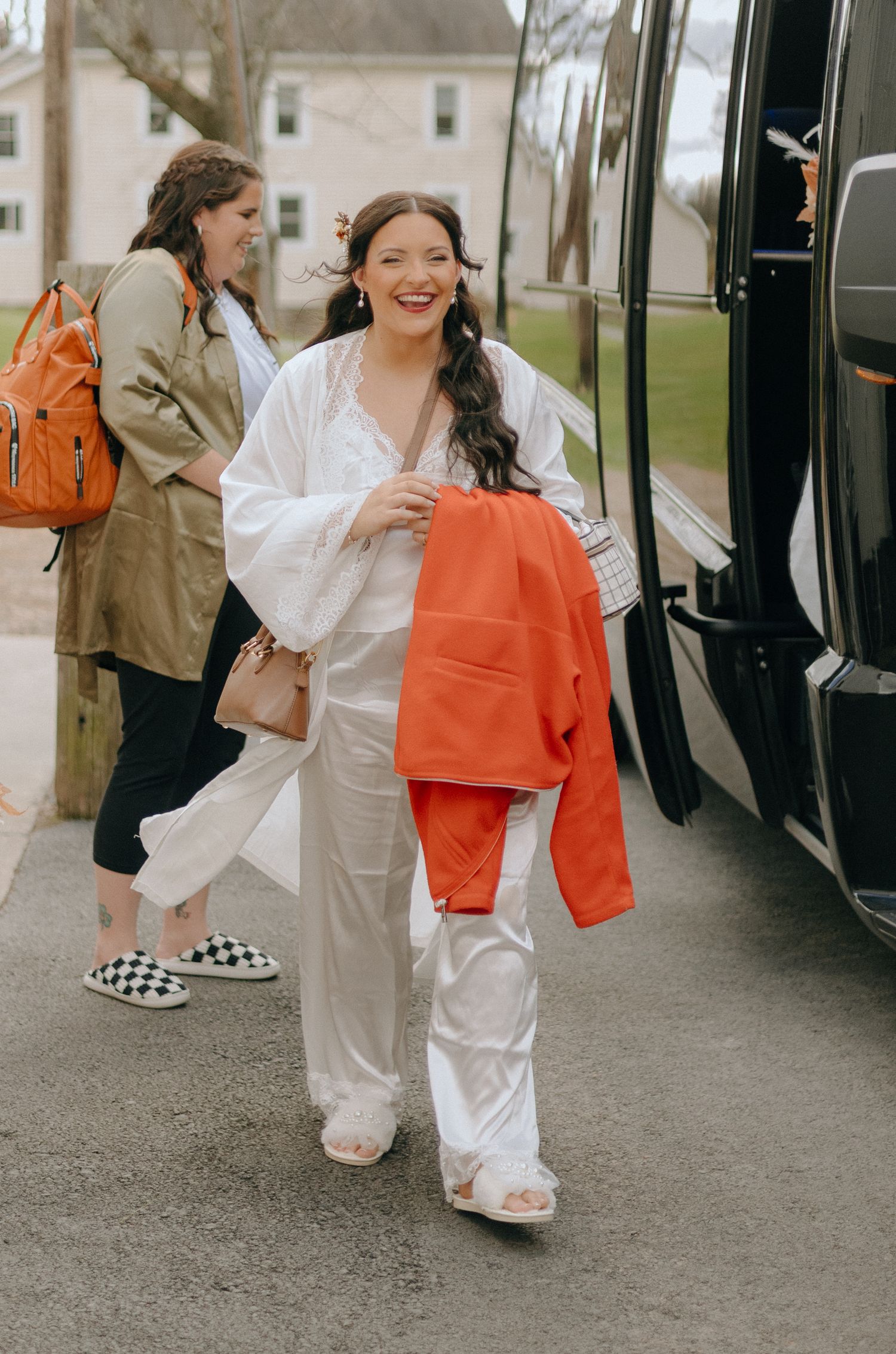 People in white outfits and orange accessories walking alongside a black vehicle.