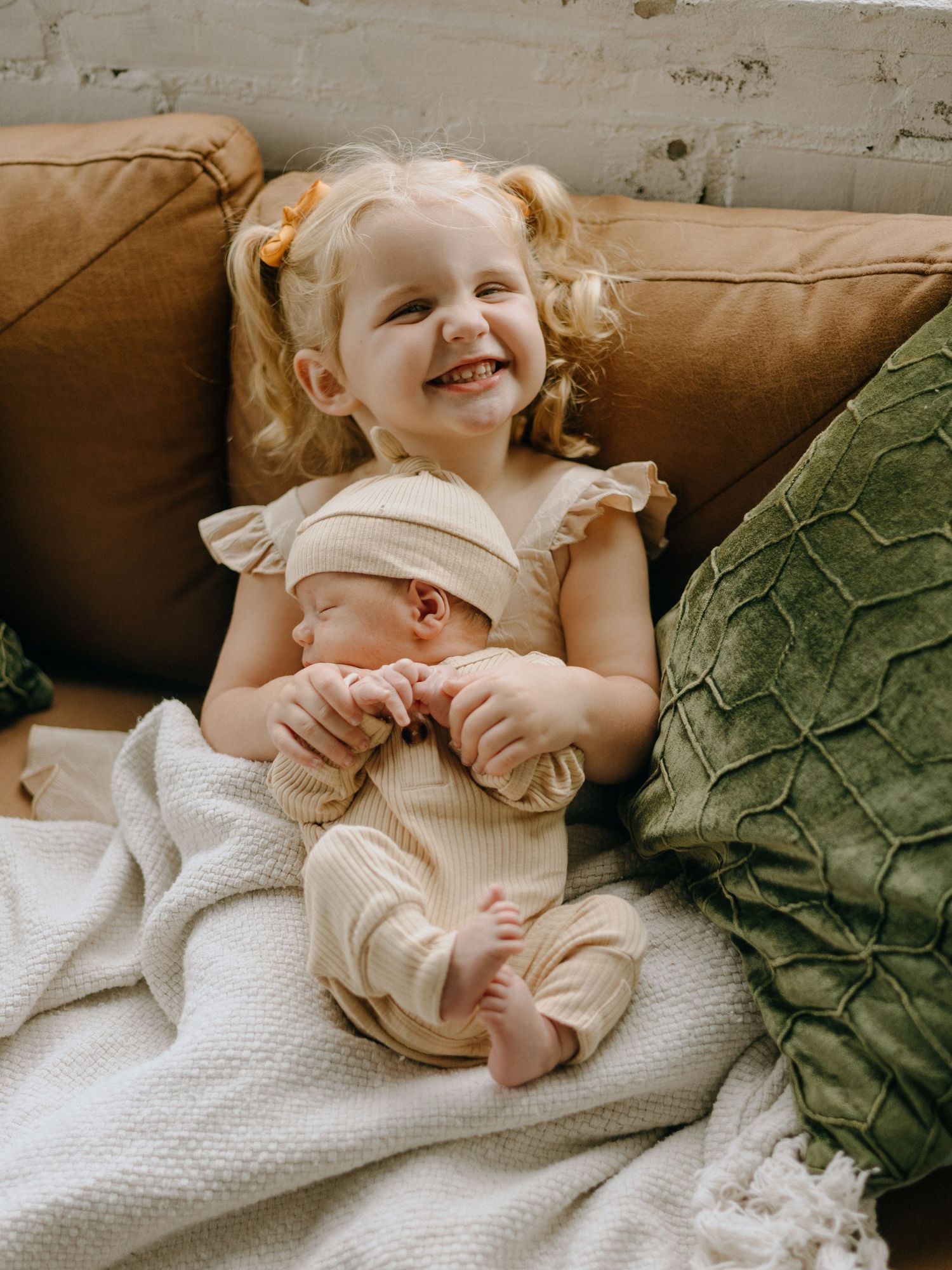A child rests on a brown couch with white blankets and a green decorative pillow.