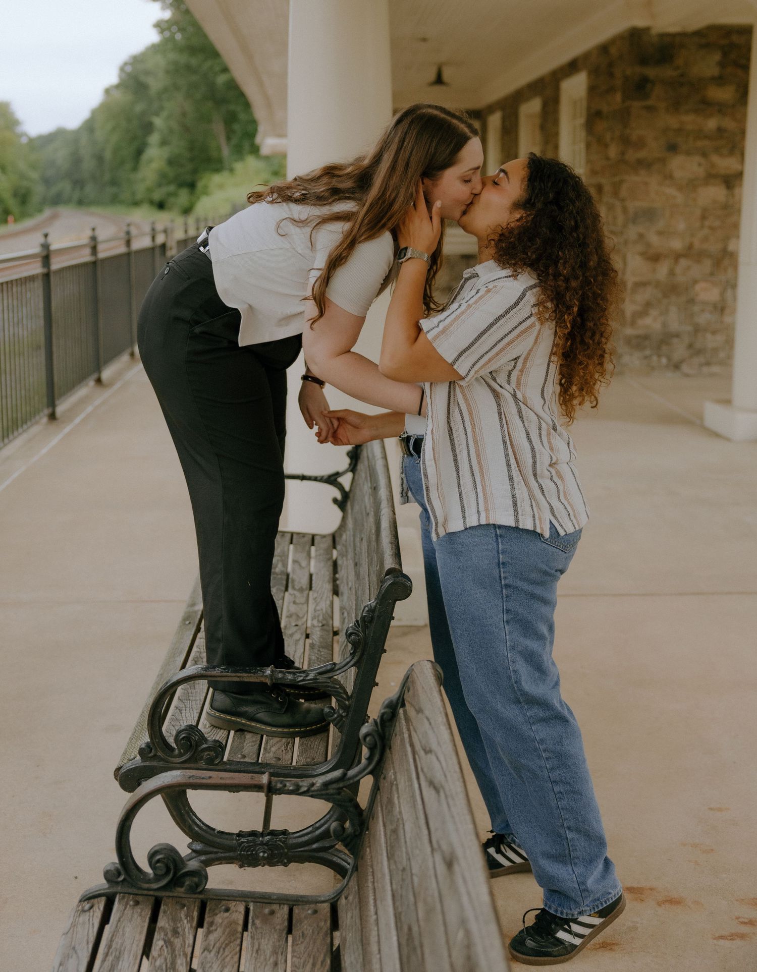 Friends sharing a playful moment on an outdoor bench near a stone building.