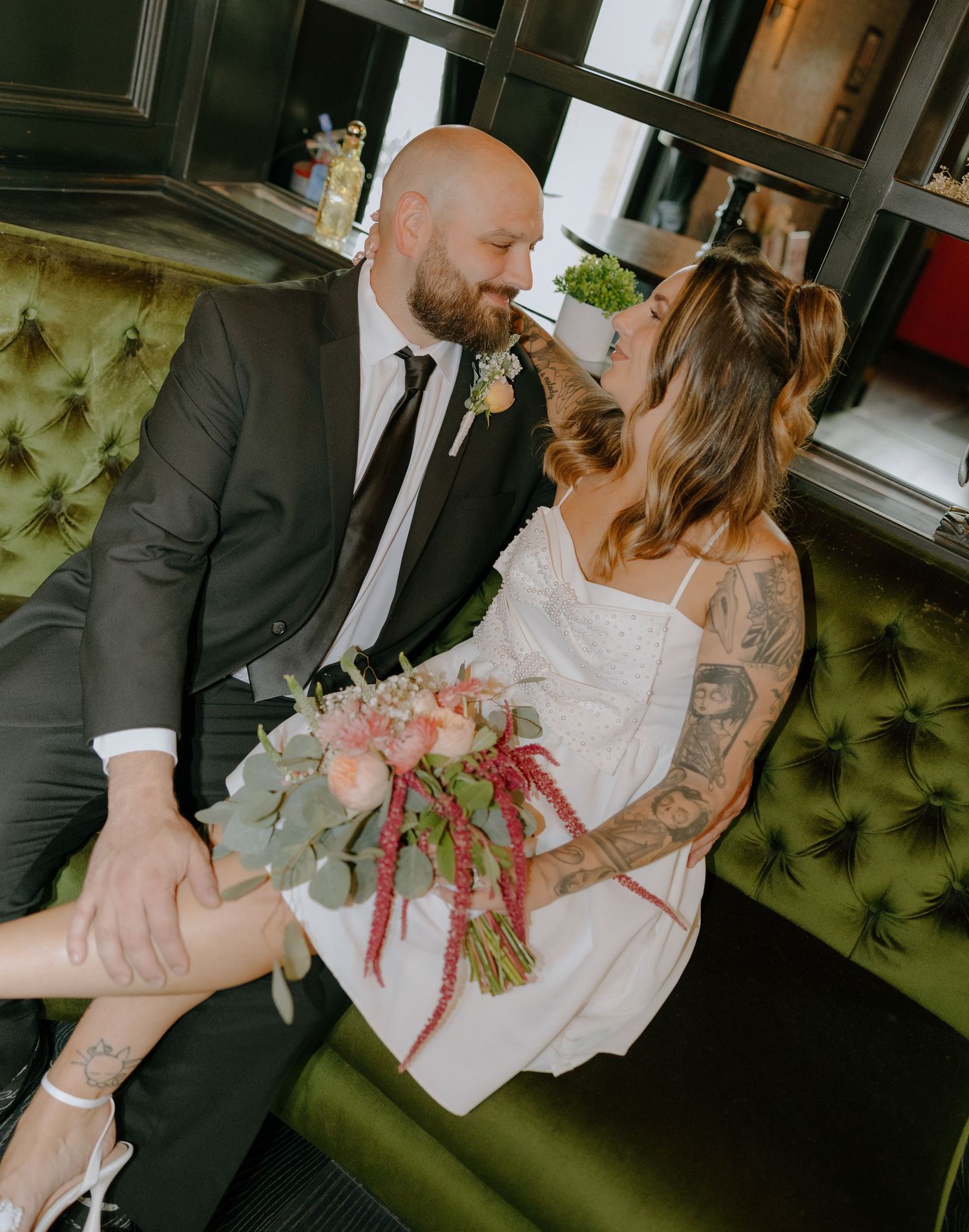 A couple shares intimate moments on a green velvet couch in an indoor setting.
