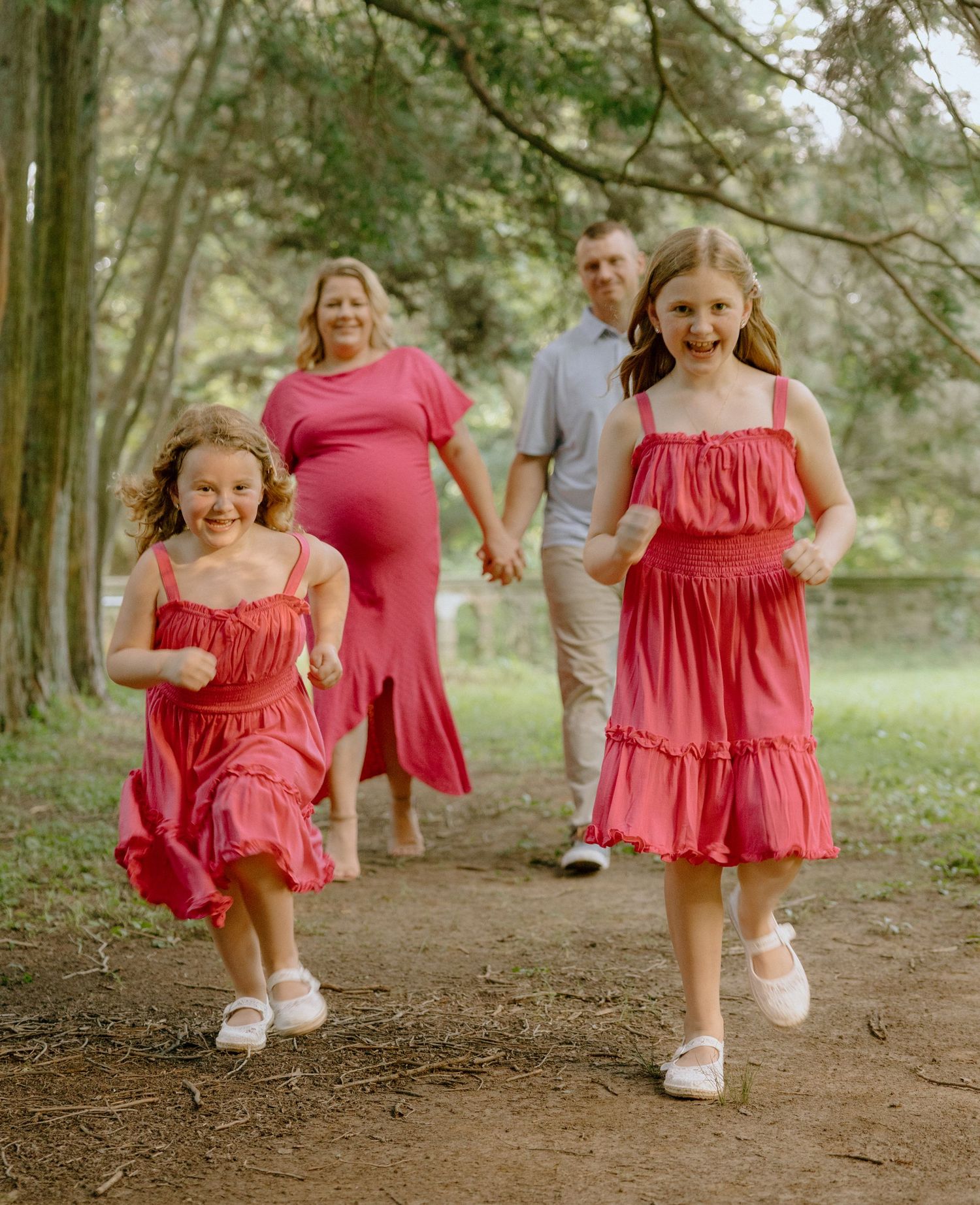 Children in red dresses running playfully down a wooded trail.