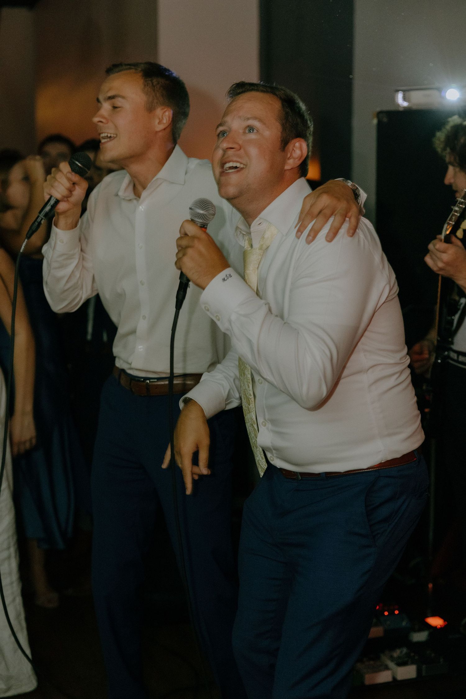 Wedding guests dancing and singing karaoke in a darkened reception venue.
