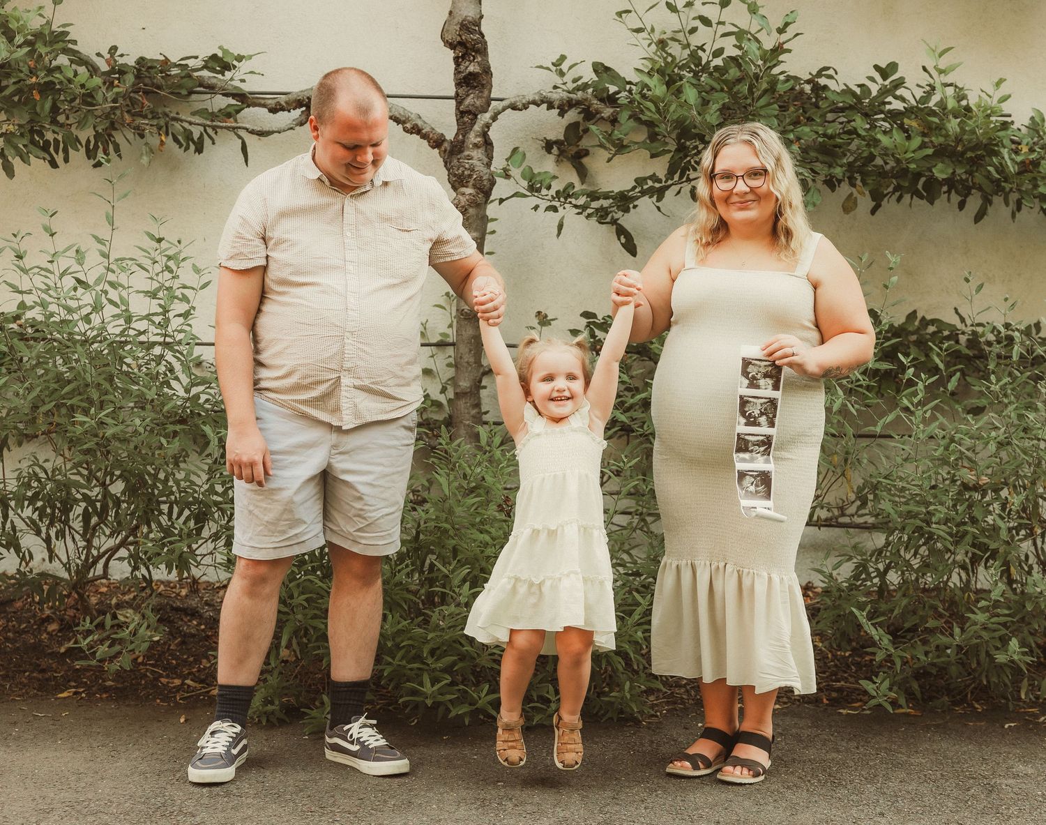 Wedding party dressed in beige and white poses casually outdoors against a neutral wall.