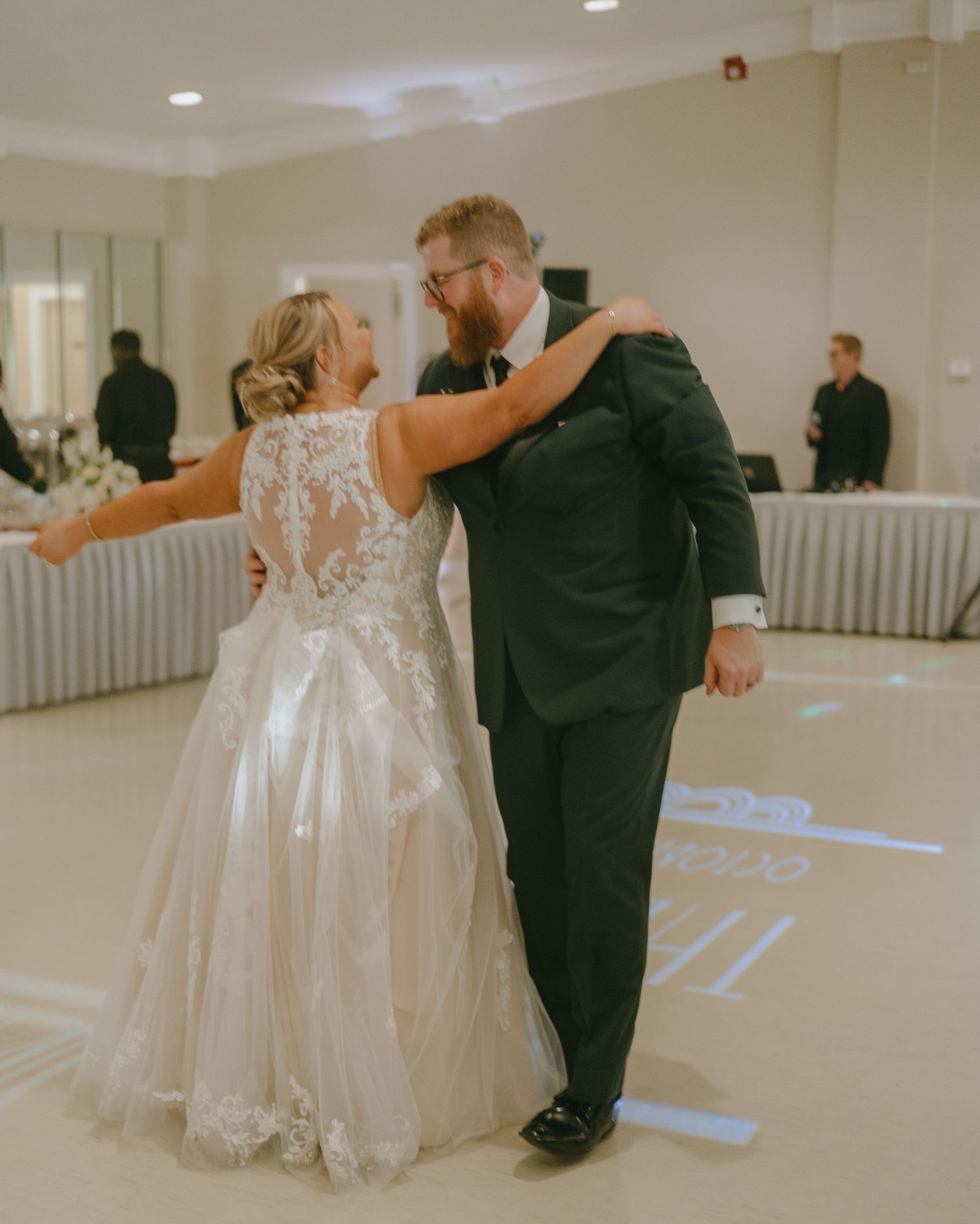 A couple shares their first dance in a reception hall with white walls and elegant decor.