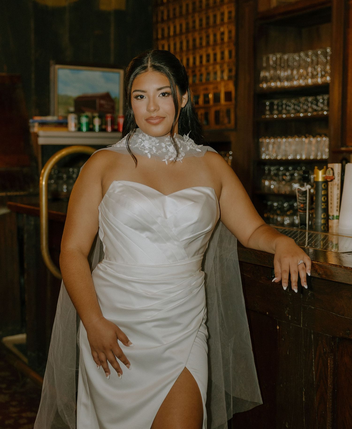 An elegant white wedding dress displayed in a vintage bar setting with wooden decor and wine glasses.
