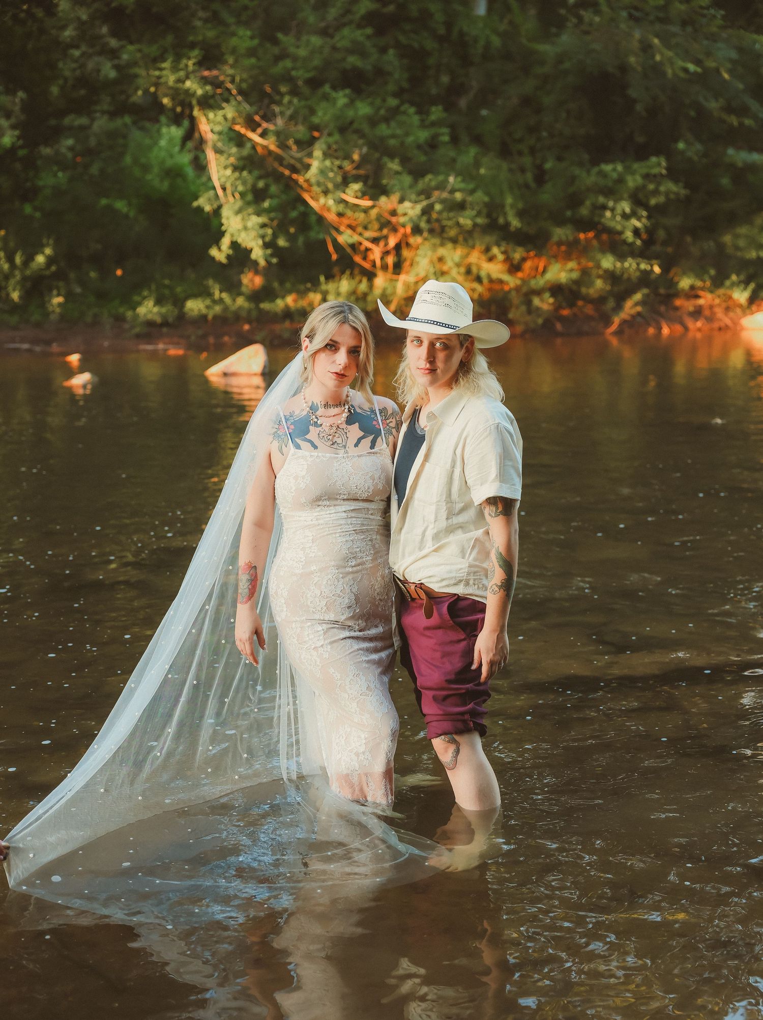 A couple wades in a river during their wedding photoshoot with autumn colors reflecting on the water.
