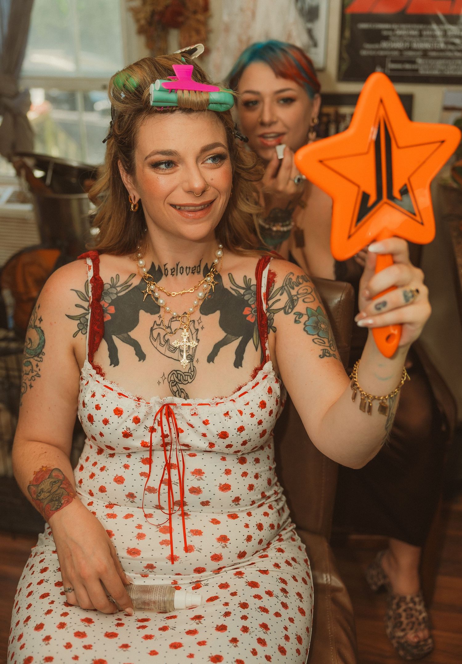 Person in a white polka dot dress with visible tattoos holding orange star decorations at a celebration.