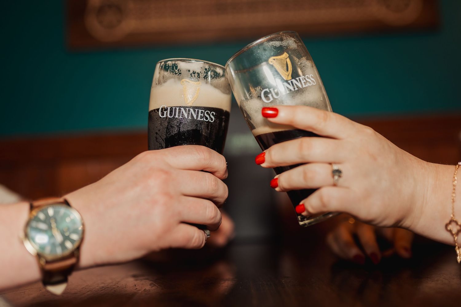Two hands toast with Guinness beer and another beverage while wearing watches and rings.