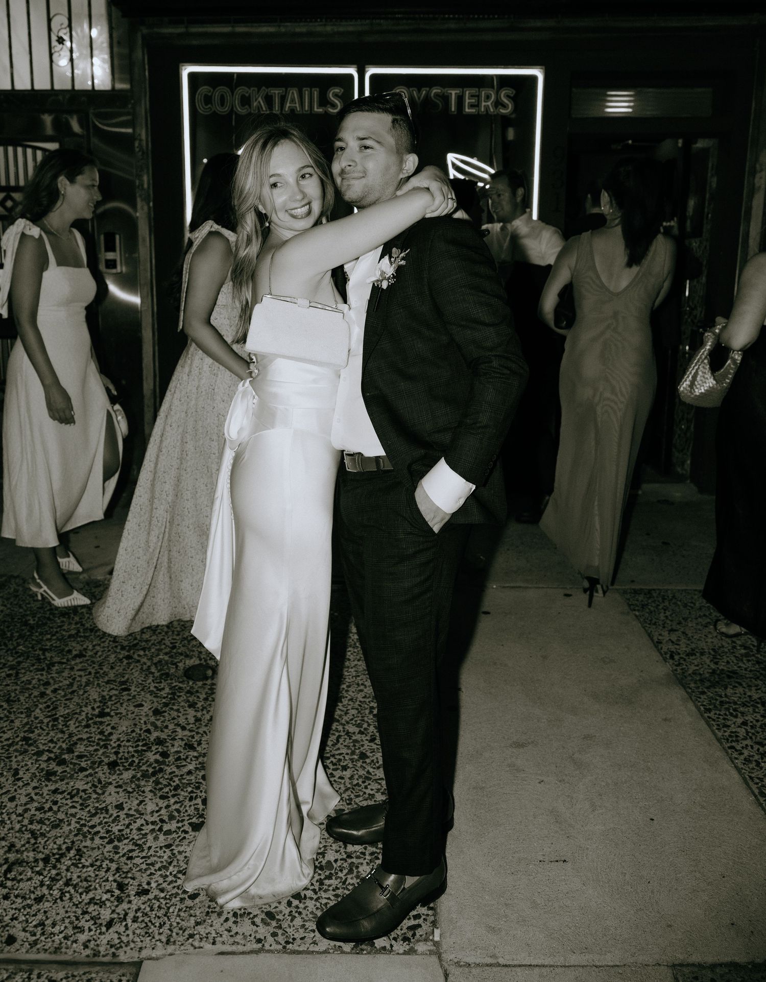 Couple dancing together at a reception venue with neon cocktail signs in the background.