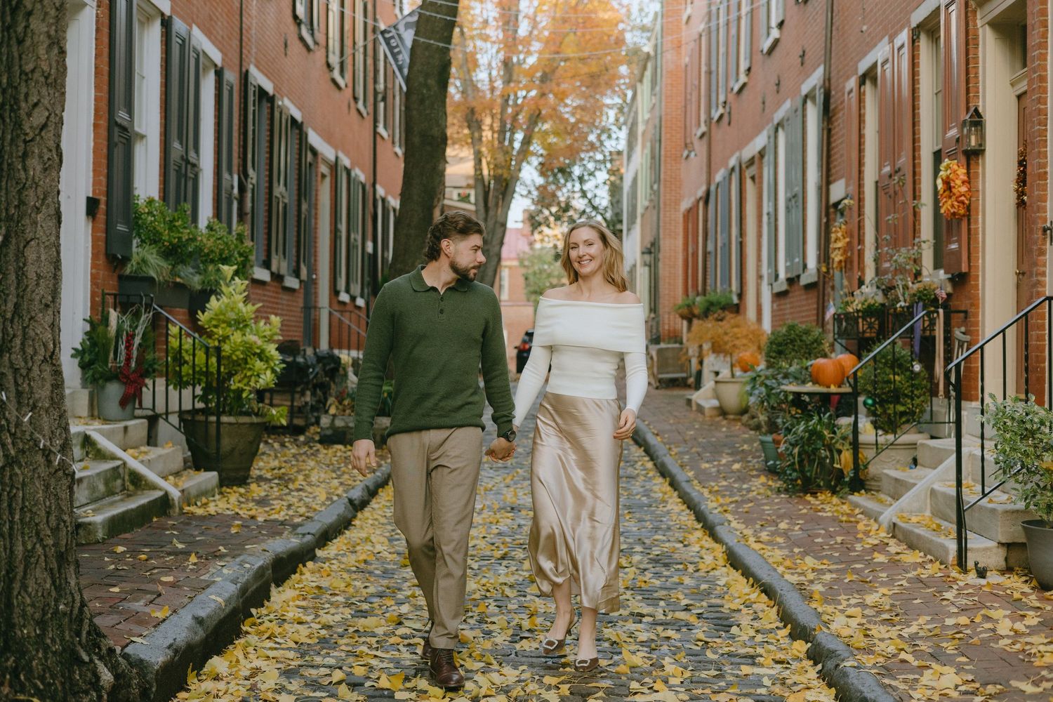 A romantic autumn scene on a brick-lined street with fallen leaves and historic buildings.