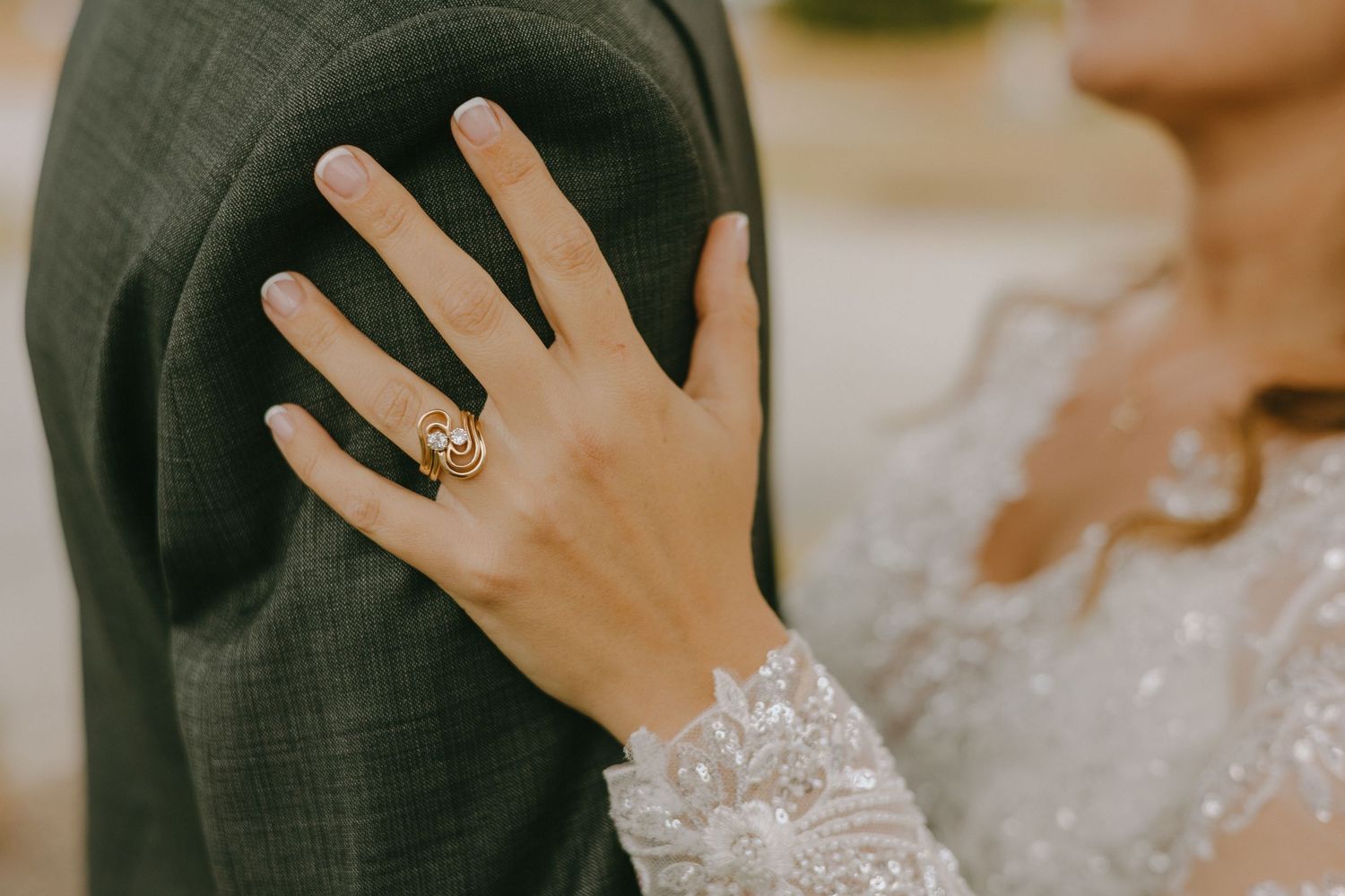A close-up of a hand wearing a delicate lace sleeve and an ornate engagement ring resting on a dark fabric.