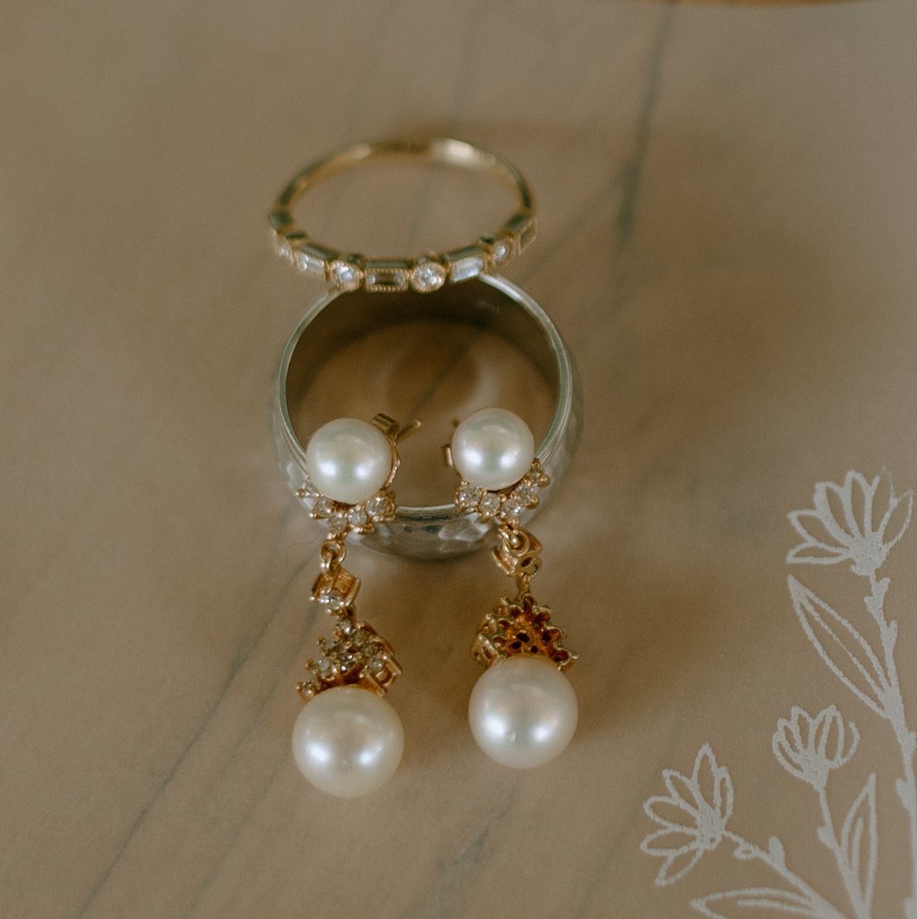 Delicate pearl and gold jewelry pieces arranged in a row showcasing rings and earrings on a neutral background.