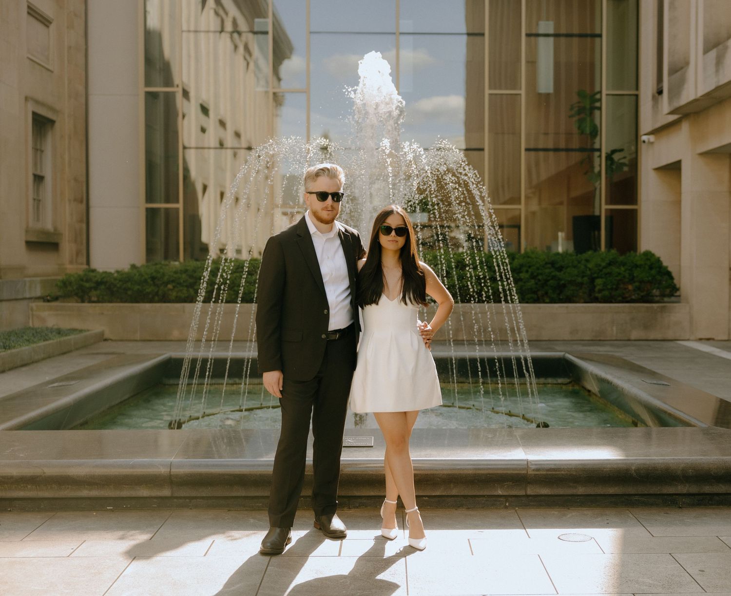 Couple walking together by a water fountain on a sunny day.