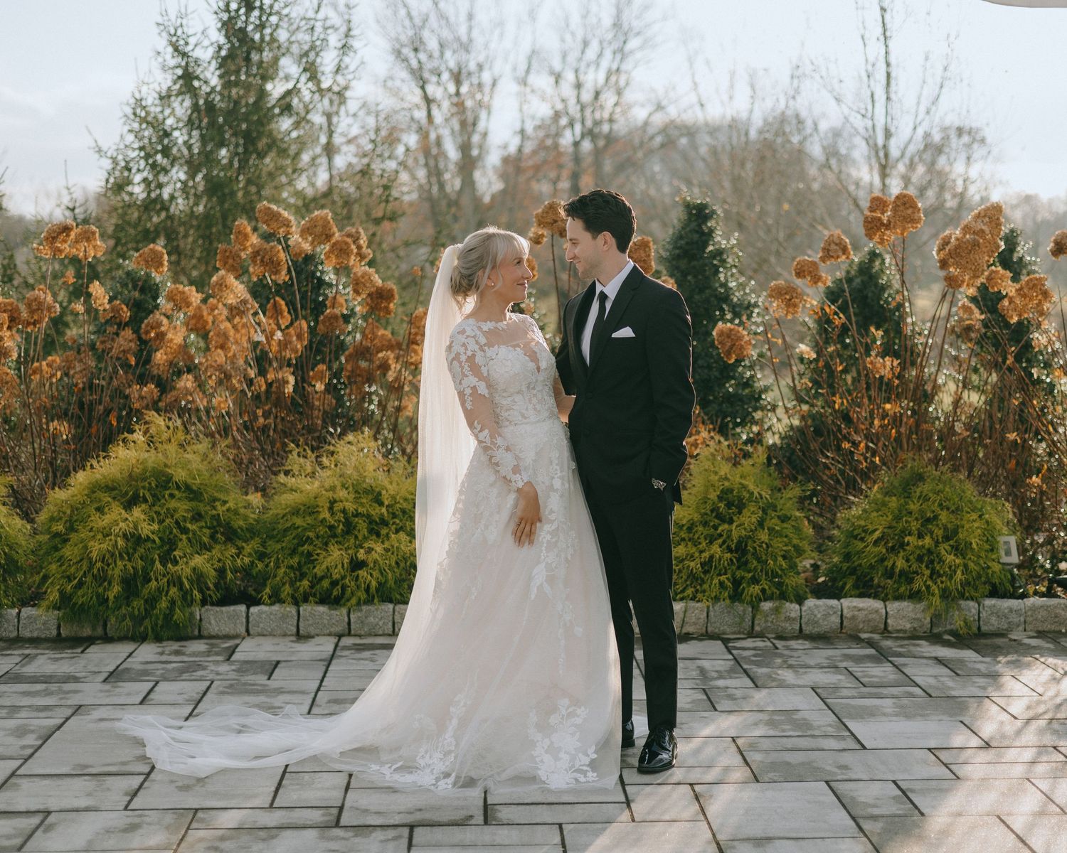 A romantic couple in wedding attire shares intimate moments on a stone terrace surrounded by autumn foliage.