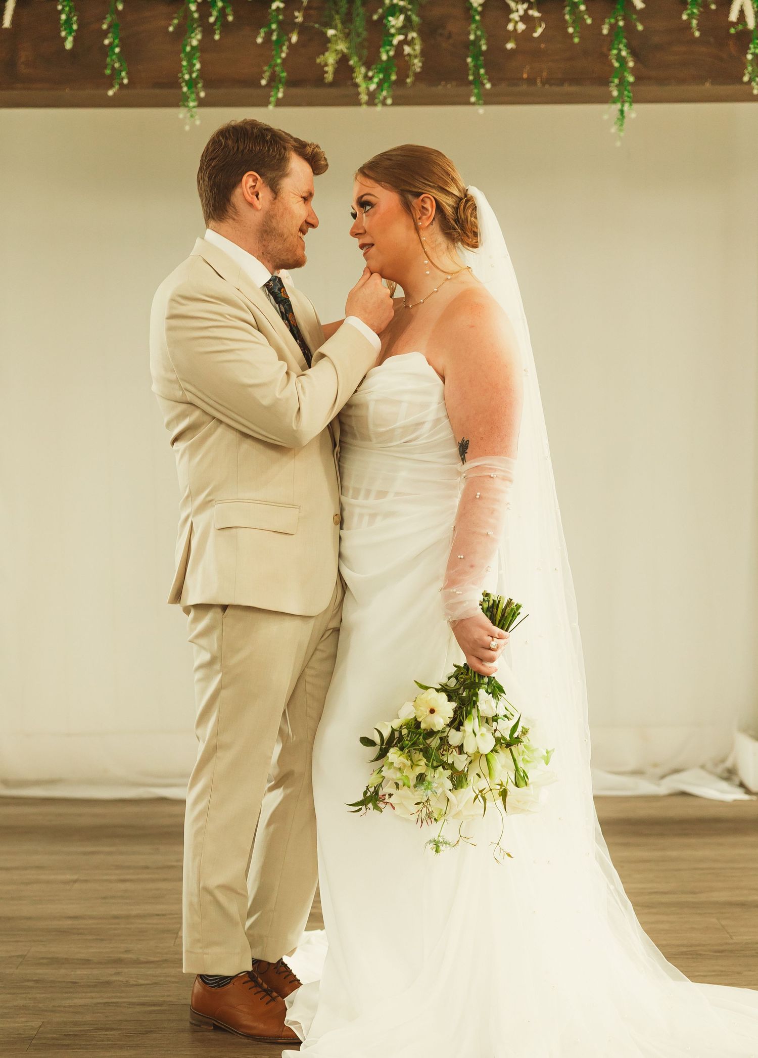 Intimate moment between newlyweds as groom tenderly cups bride's face during outdoor wedding ceremony.