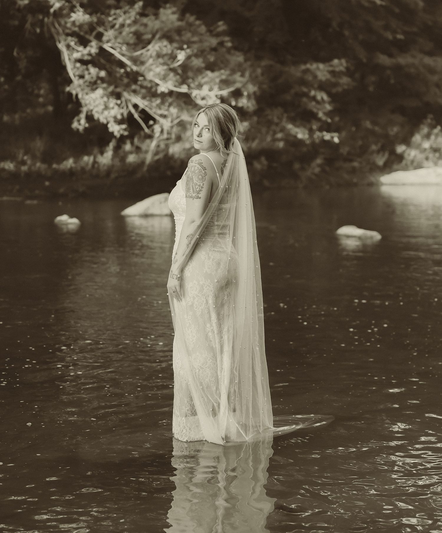 A vintage-style black and white photo shows a flowing wedding dress in rippling water.