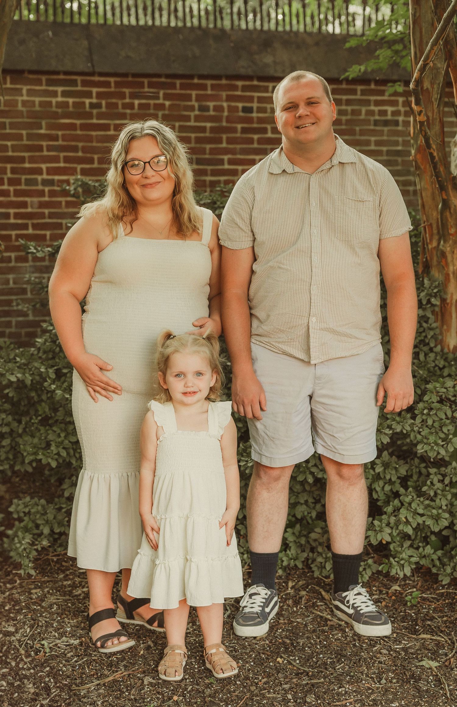 Family wearing coordinated cream and beige outfits poses against brick wall in outdoor setting.