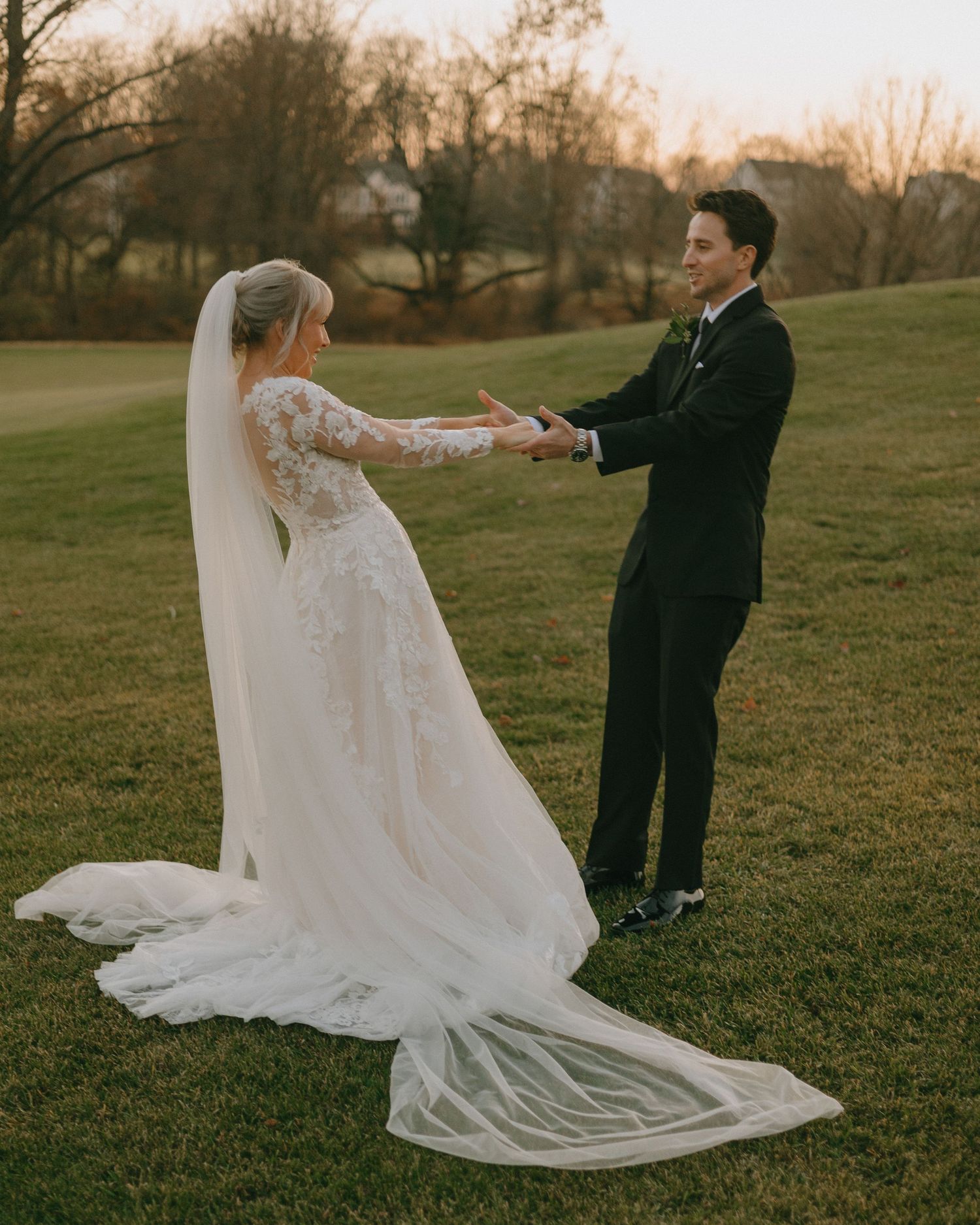 A couple dances on grass during golden hour, with the bride's veil flowing elegantly in the breeze.