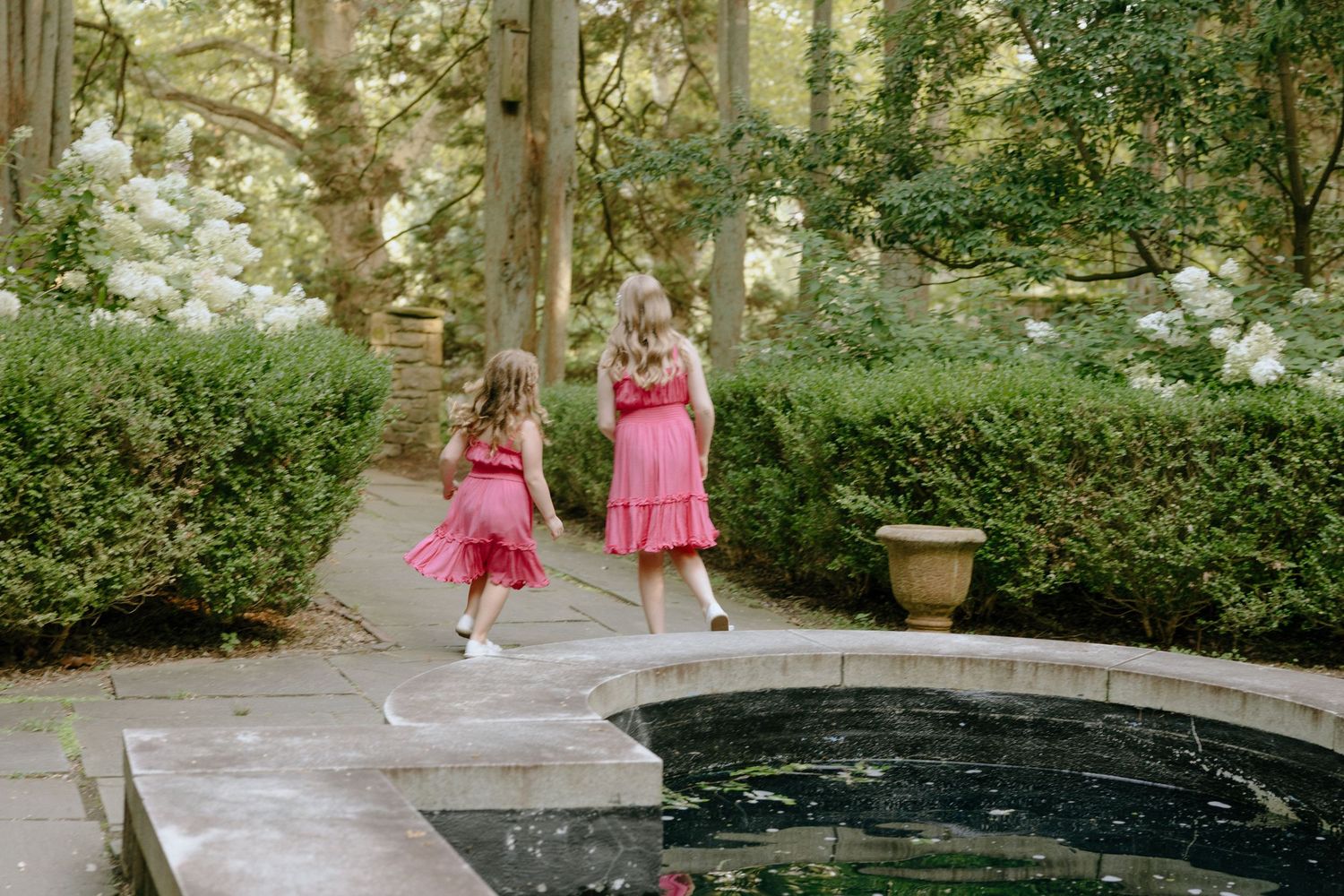 People walking along a curved garden path near a reflective pool on a sunny day.