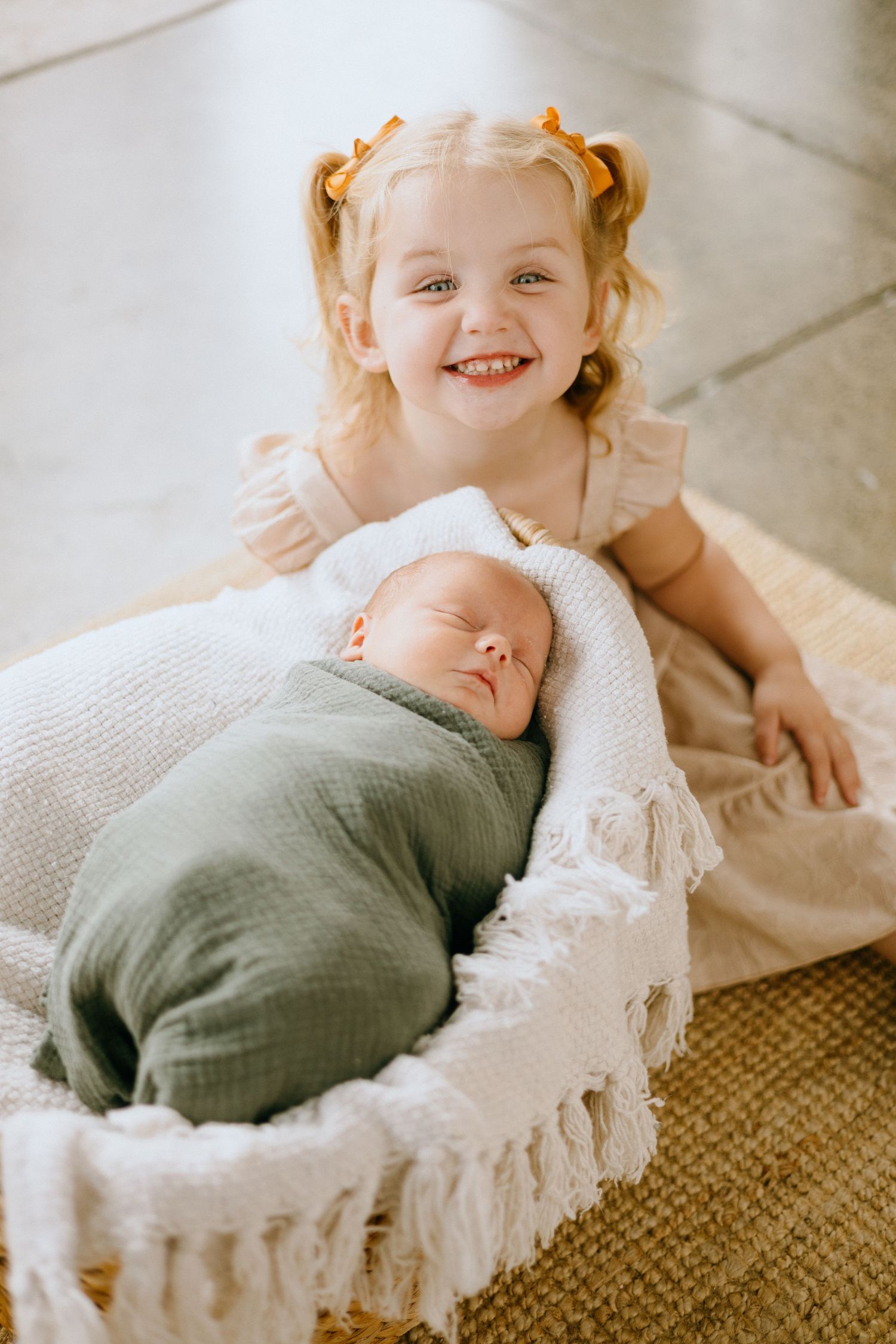 A child in a white dress lies on a textured brown rug with a soft cream blanket.