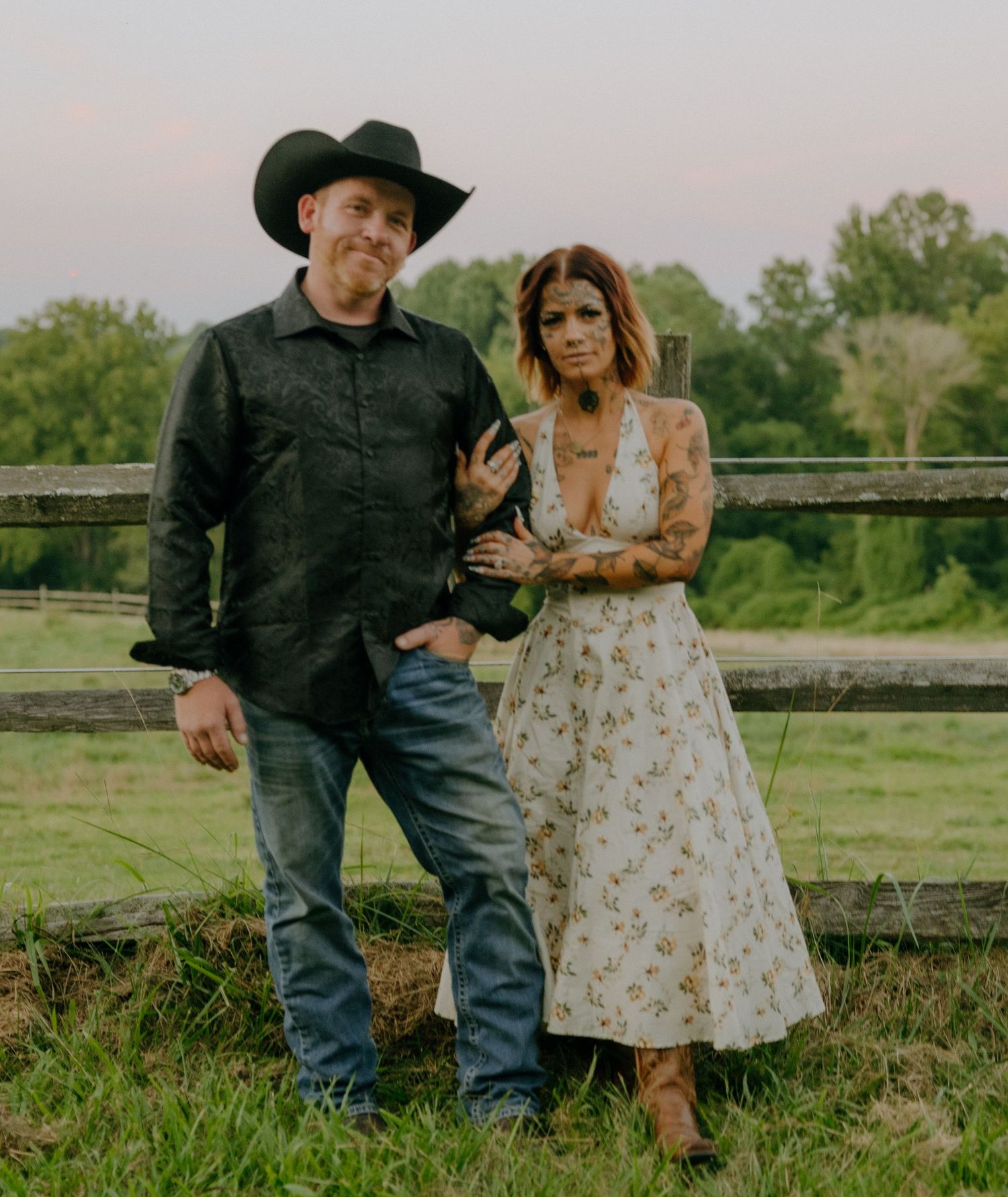 Romantic countryside photoshoot with couple by rustic wooden fence at sunset.