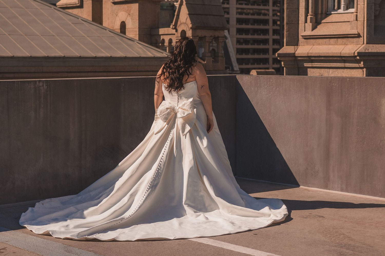 Elegant bridal portrait showcasing dramatic train of white wedding gown on rooftop setting.