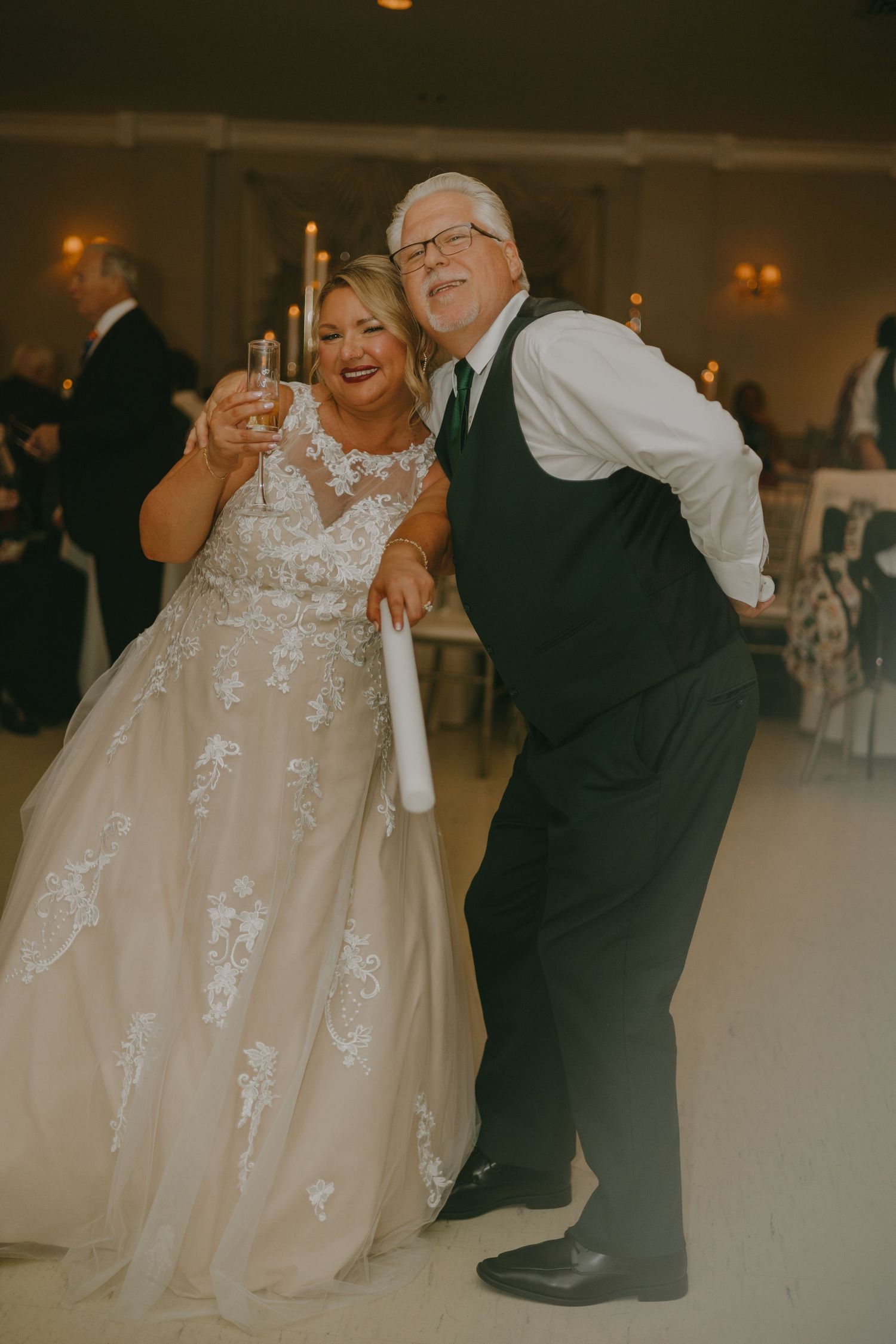 A pair dancing together at a wedding reception, with the bride wearing an elegant lace gown.