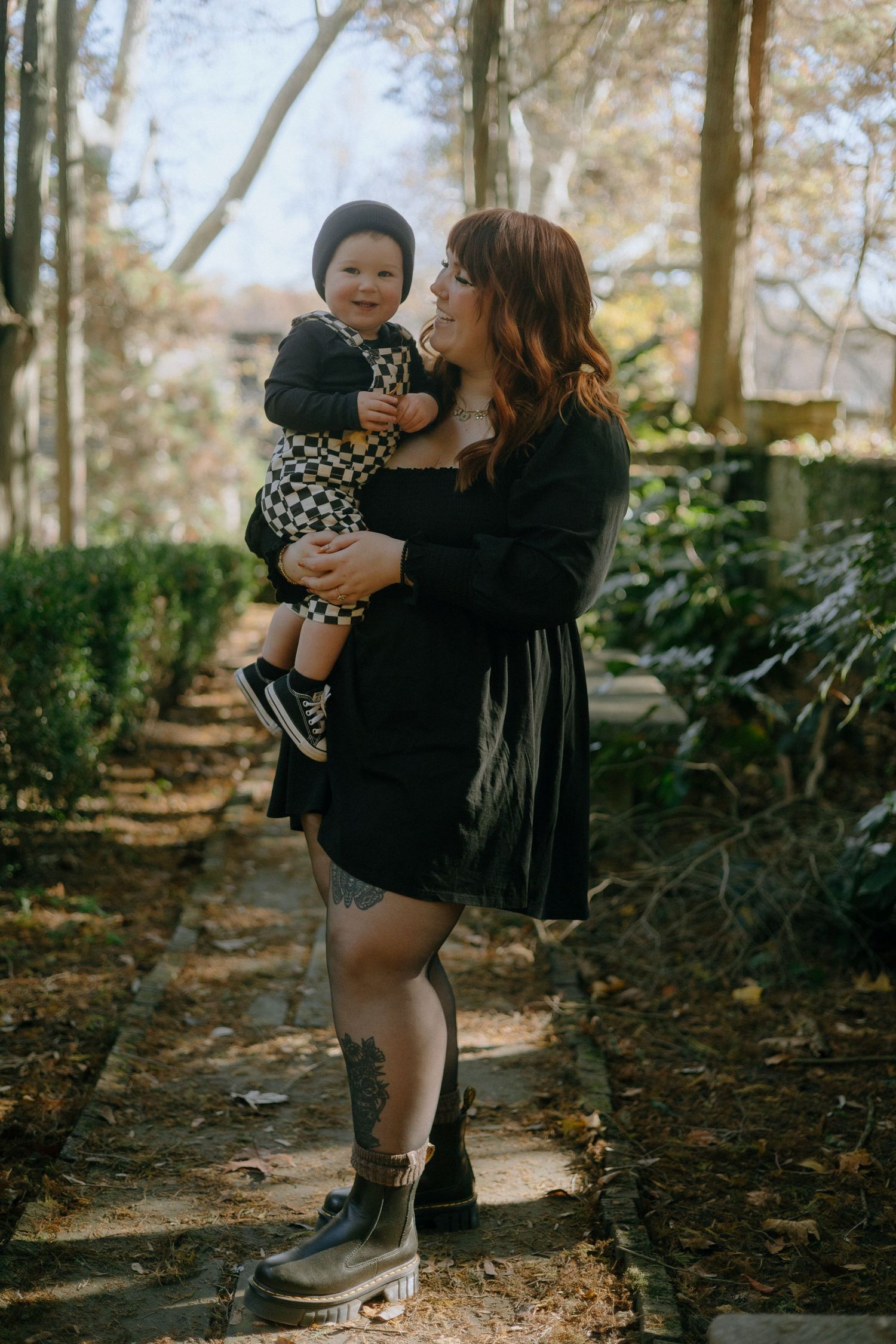 A tender autumn moment outdoors with a baby in checkered clothing among fall foliage and stone walls.