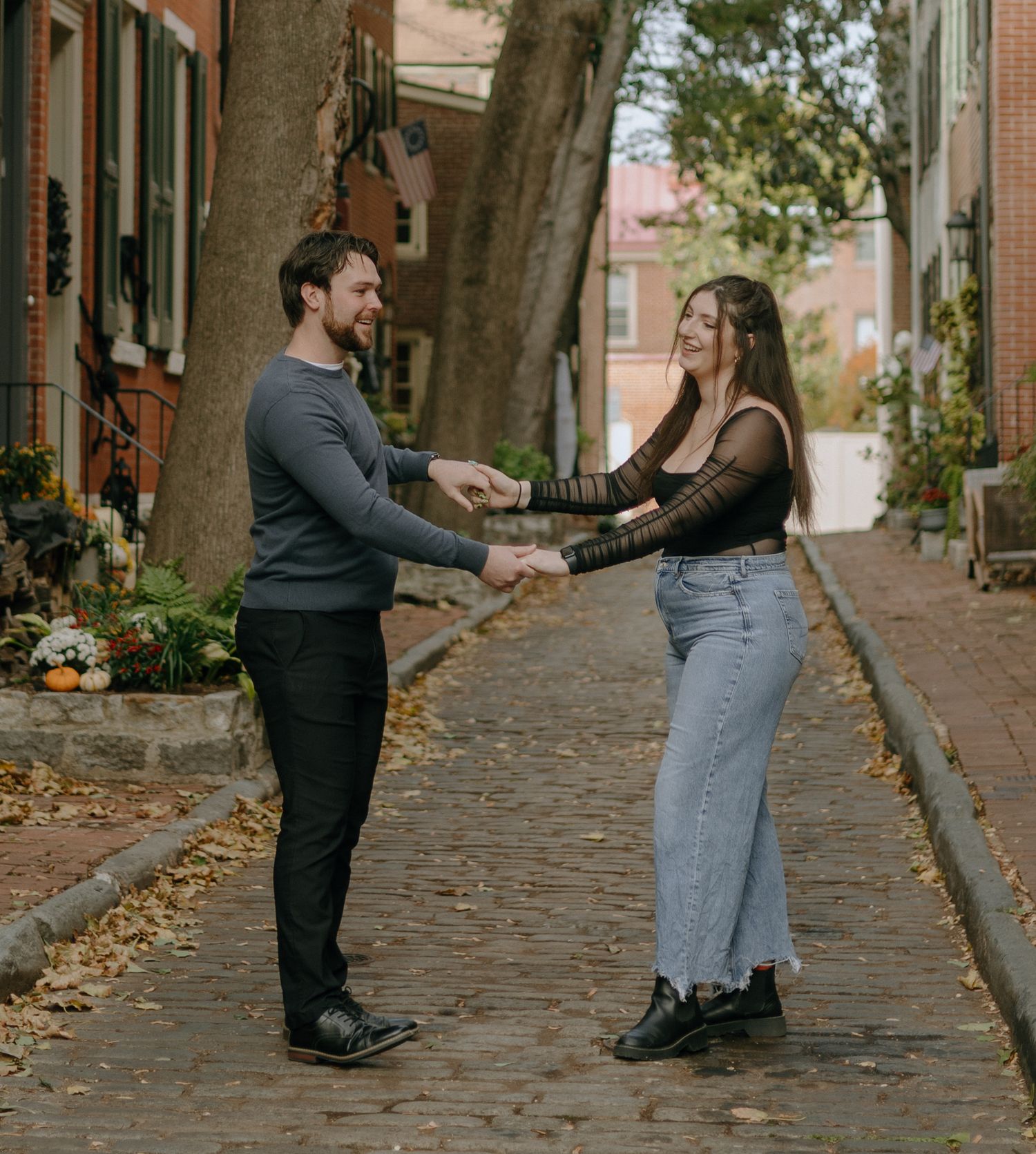 Couple dancing and laughing together on a cobblestone street during an autumn day.