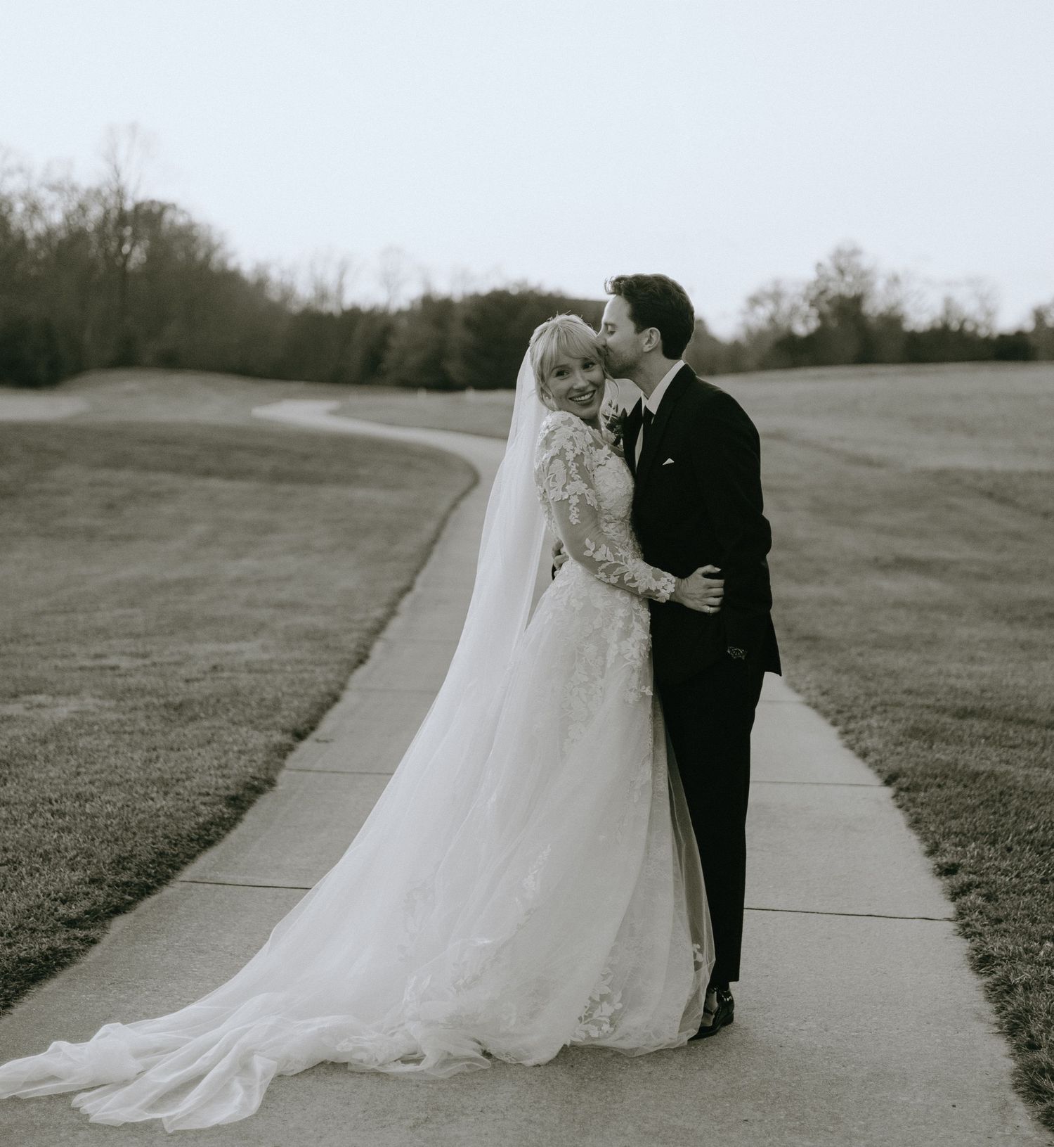 Black and white wedding photos showing a couple in formal attire walking along an outdoor path surrounded by grass.